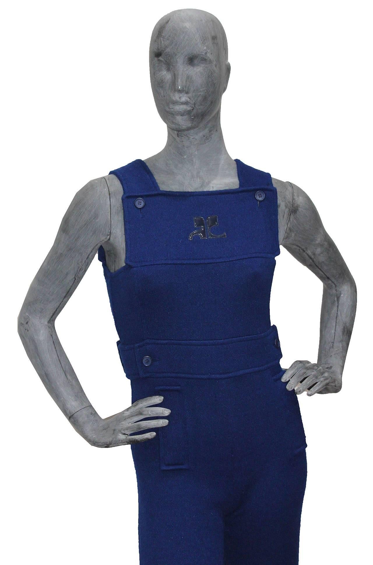 A 1971 Courreges Paris jumpsuit in the style of dungarees. The jumpsuit has flared trousers, side metal zip closure, two front decorative pockets and waist belt. The iconic 1960s patent 'AC' (Andre Courreges) logo features on the front of the