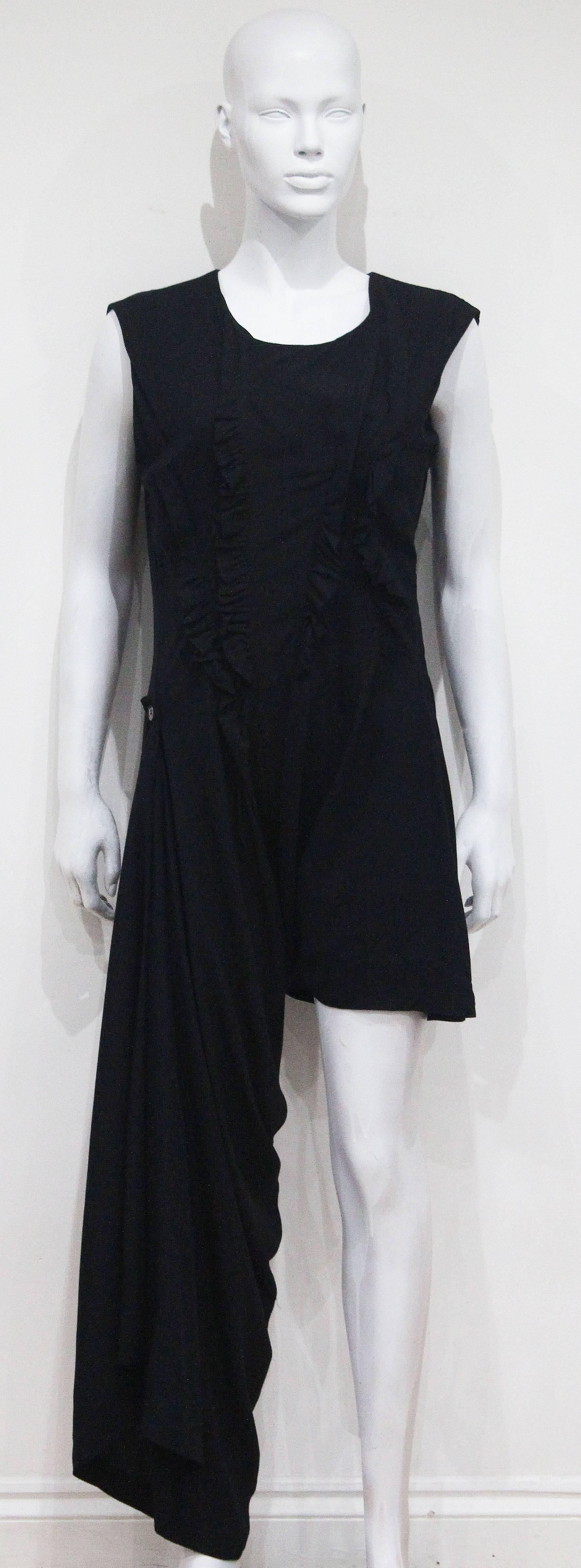 An early COMME des GARCONS asymmetric jumpsuit from the 1980s. The garment has a wrap design which ties under the leg and fastens with a button on the side of the hip to create one long leg and one short alternatively the dress can also be styled as