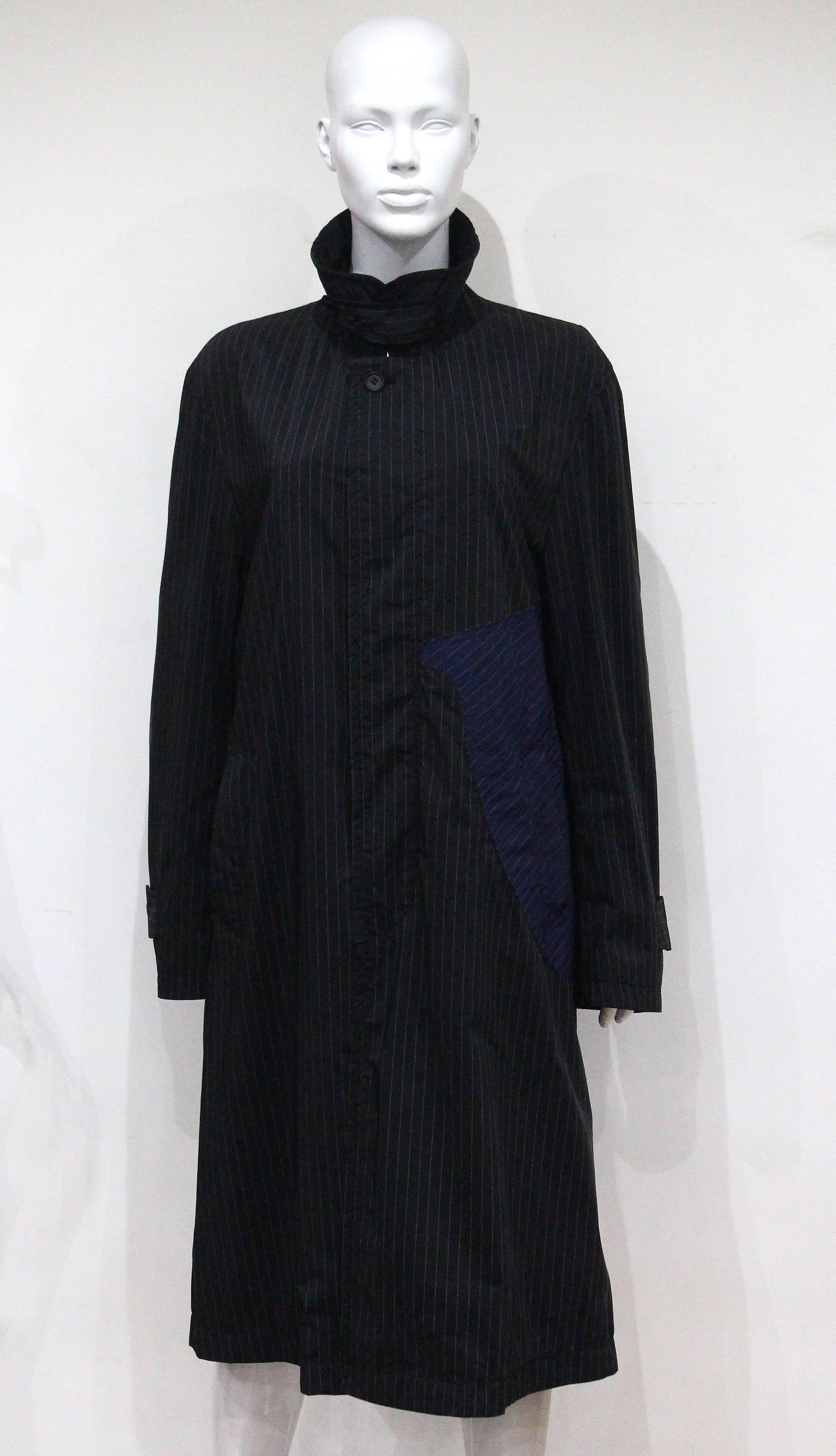 Der Issey Miyake Windbreaker-Mantel aus den 1990er Jahren zeichnet sich durch ein Nadelstreifendesign mit einer schwarzen Basis und ausgeschnittenen Einsätzen in Marineblau aus. 

Unisex