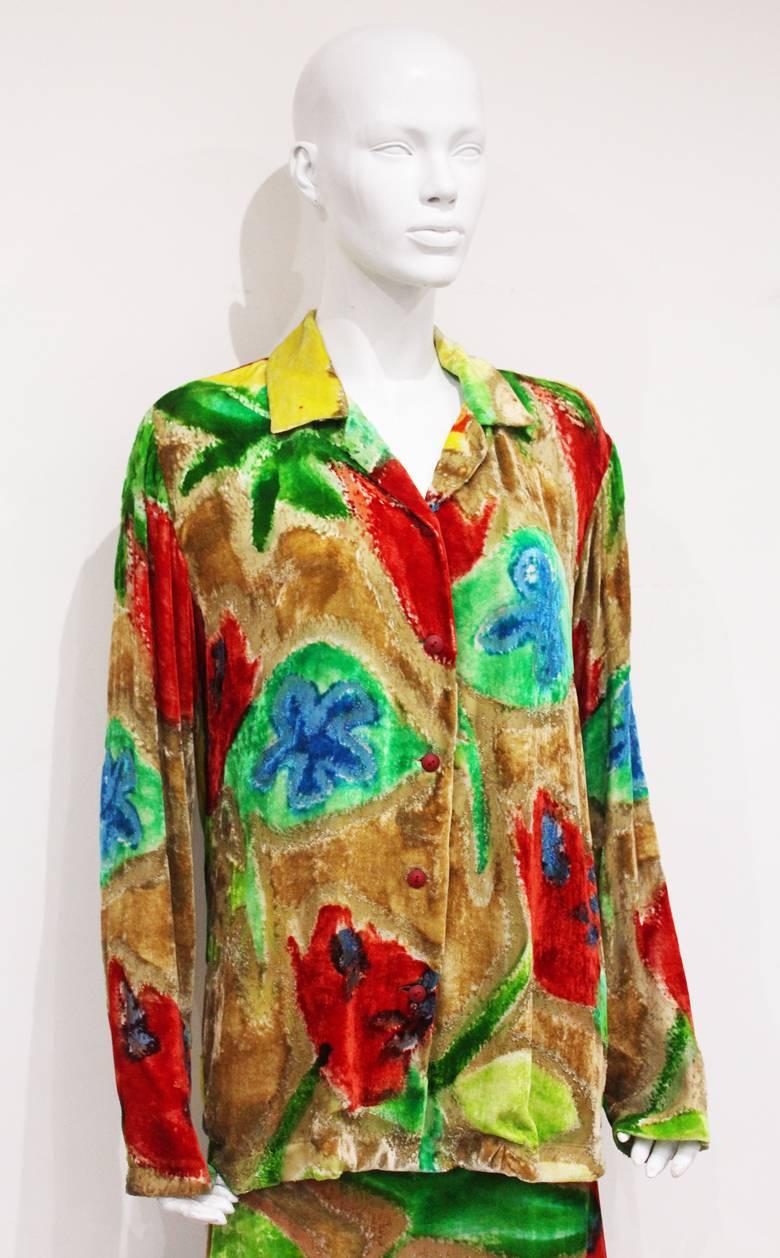 Issey Miyake skirt suit from the 1990s. The suit is in a velvet devoré and has a vibrant abstract floral print. The blouse is oversized and has button closures running through the centre. The skirt is full length and has a red silk lining which