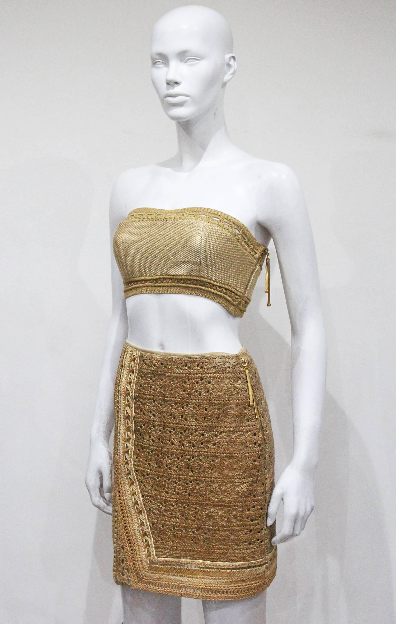 A Gianfranco Ferre skirt and bustier ensemble from the Spring/Summer 2001 season. The ensemble is in a woven raffia with assets of knitted crochet. The bustier has a built in bra and gold metal tassel zipper on one side. The skirt is in the fitted
