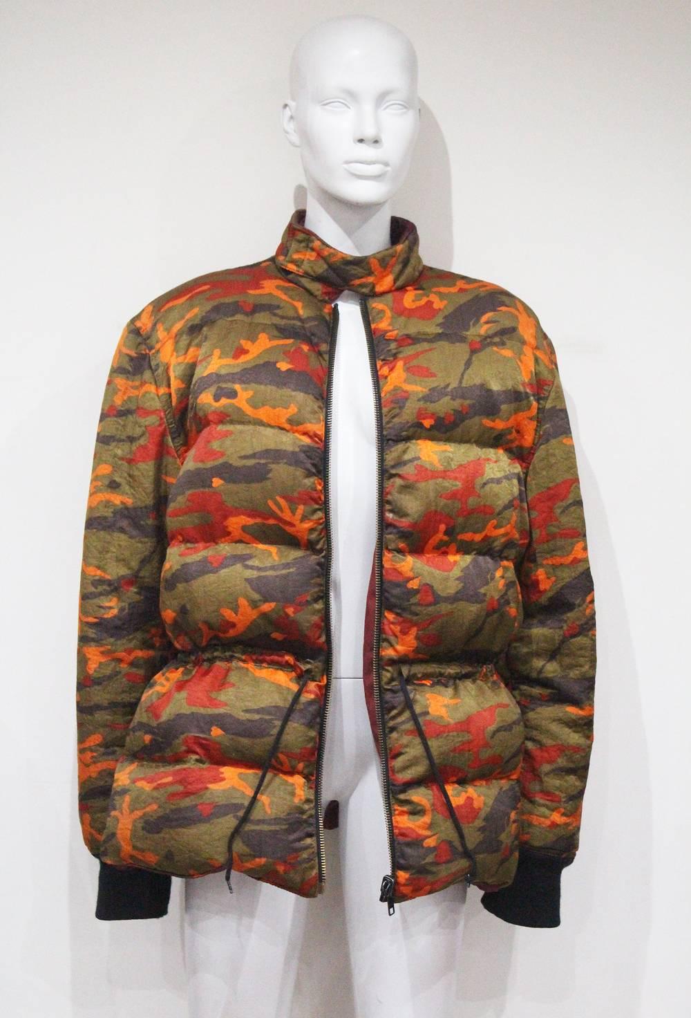 An oversized Junior Gaultier puffa jacket designed by Jean Paul Gaultier in the early 1990s. The puffa jacket with orange camo print features large padded quilts, knitted cuffs, zip closure, drawstring waist, and maroon double lining.

Large