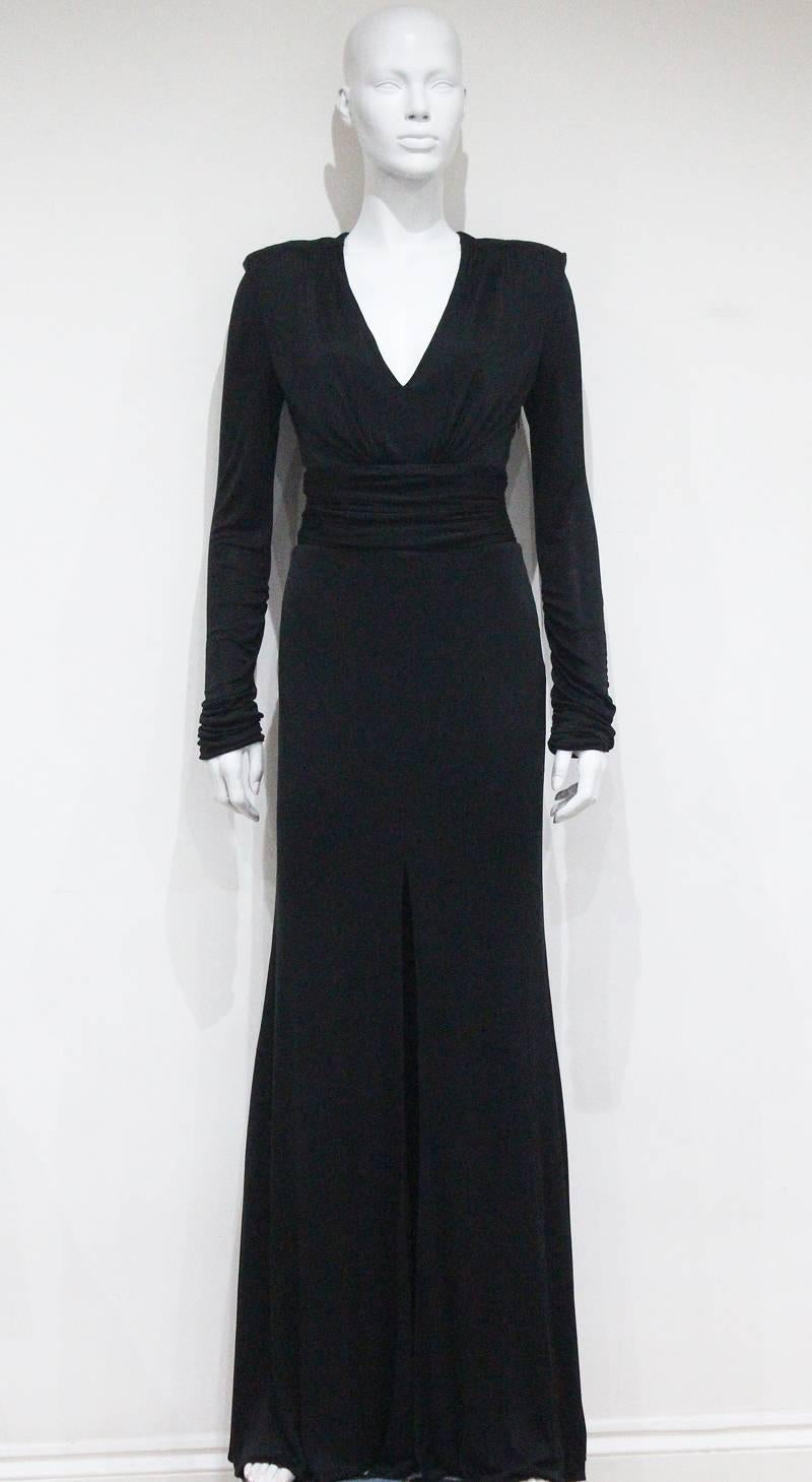 A Gianni Versace Couture evening dress in black silk jersey. The dress features a high central leg slit, draped waist, shoulder pads and v-neck plunge. 

It 42 - Fr 38