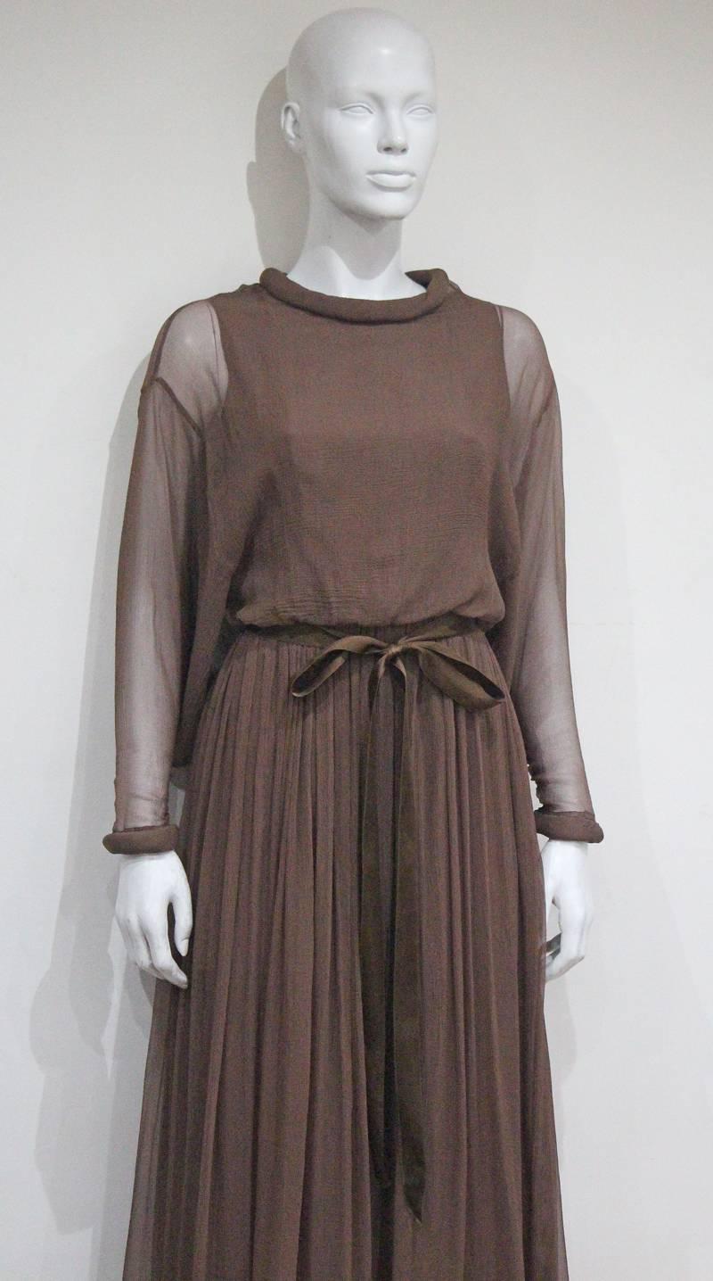 An early 1970s Jean Varon evening dress in taupe chiffon. The dress feathers tube like collar and cuffs, bat-wing design and silk belt. 

Approx. Fr 38