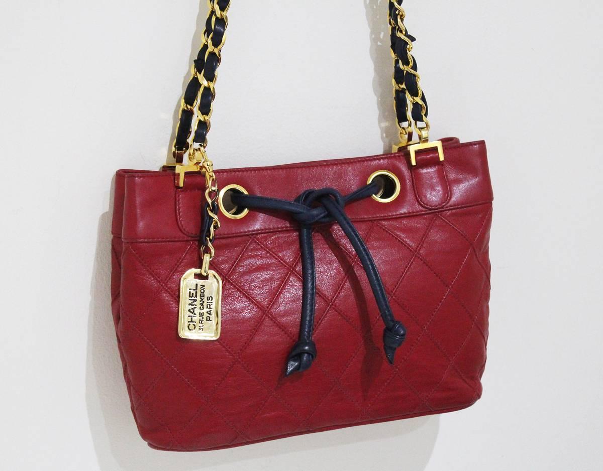 Chanel drawstring bag dating between 1986-88 and in flawless condition. The bag is in a colour block design of quilted red lambskin leather and a navy blue leather woven chain and drawstring. The bag also features a gold key chain with 'Chanel - 31