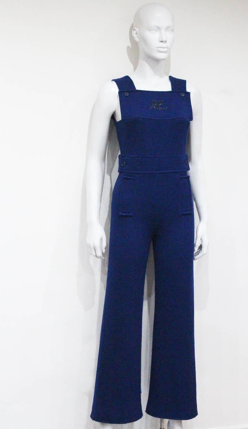 1971 Courreges Paris jumpsuit in the style of dungarees. The jumpsuit has flared trousers, side metal zip closure, two front decorative pockets and waist belt. The iconic patent 'AC' (Andre Courreges) logo featured on the front of the jumpsuit
