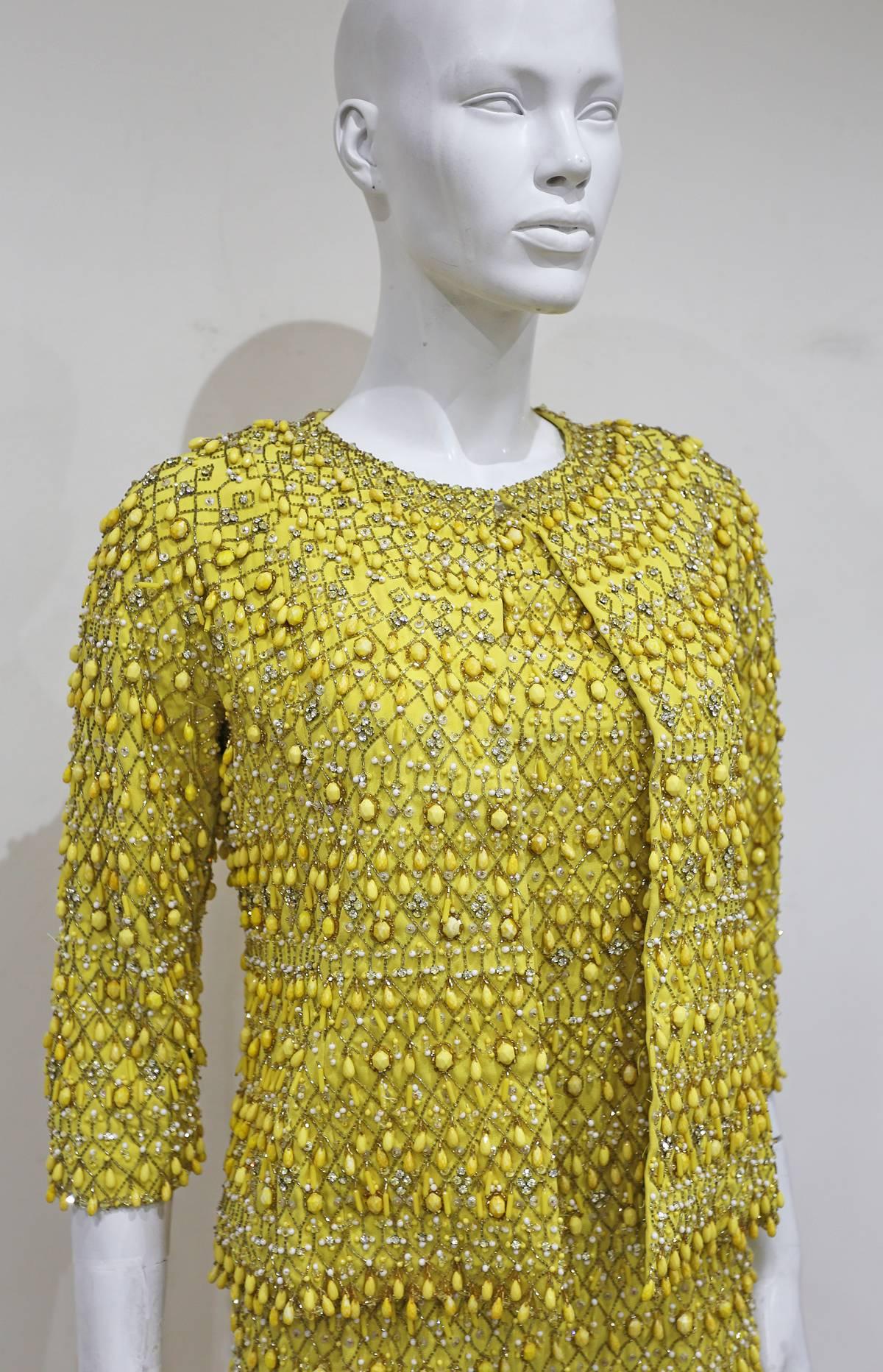 Late 1960´s haute couture evening ensemble in yellow, sleeveless dress has a V-neck at the Back and a side slit, long sleeve jacket, embroidered with rhinestones and glass-paste beads. The richness of the colour and materials contrasts with the
