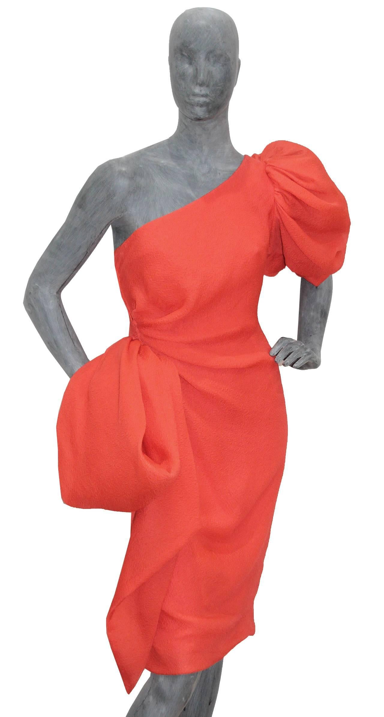 This is a beautiful asymmetric cocktail dress designed by the great Hubert de Givenchy, the dress is in his signature coral colour in a 100% silk crêpe and features a ballon sleeve and an extravagant bow which folds to the front. 

This dress was