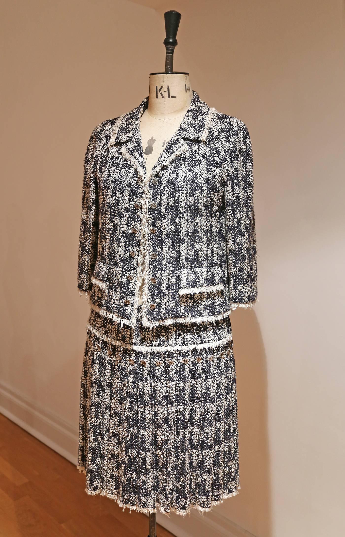 A beautiful Chanel skirt suit in metallic navy boucle tweed. The suit features and open jacket with frayed edges, silver Chanel coins and cropped sleeves and a pleated skirt which sits on the hip also with silver Chanel coins. The suit is lined in