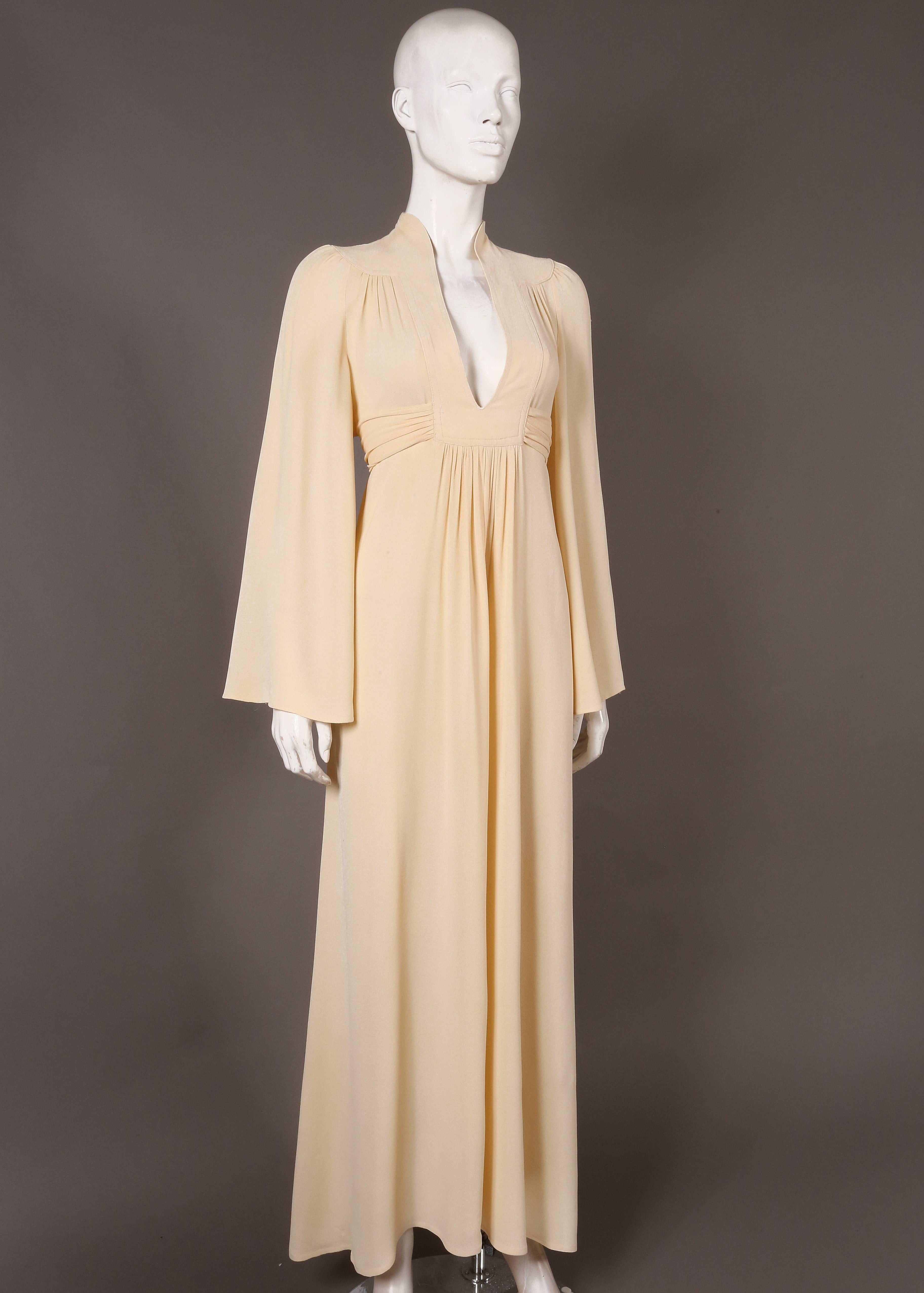 Ossie Clark for Radley cream moss crepe gown, circa 1970s. The dress features low plunge cleavage, bell sleeves, pleating throughout and a waist belt which fastenings at the rear. 

Medium
