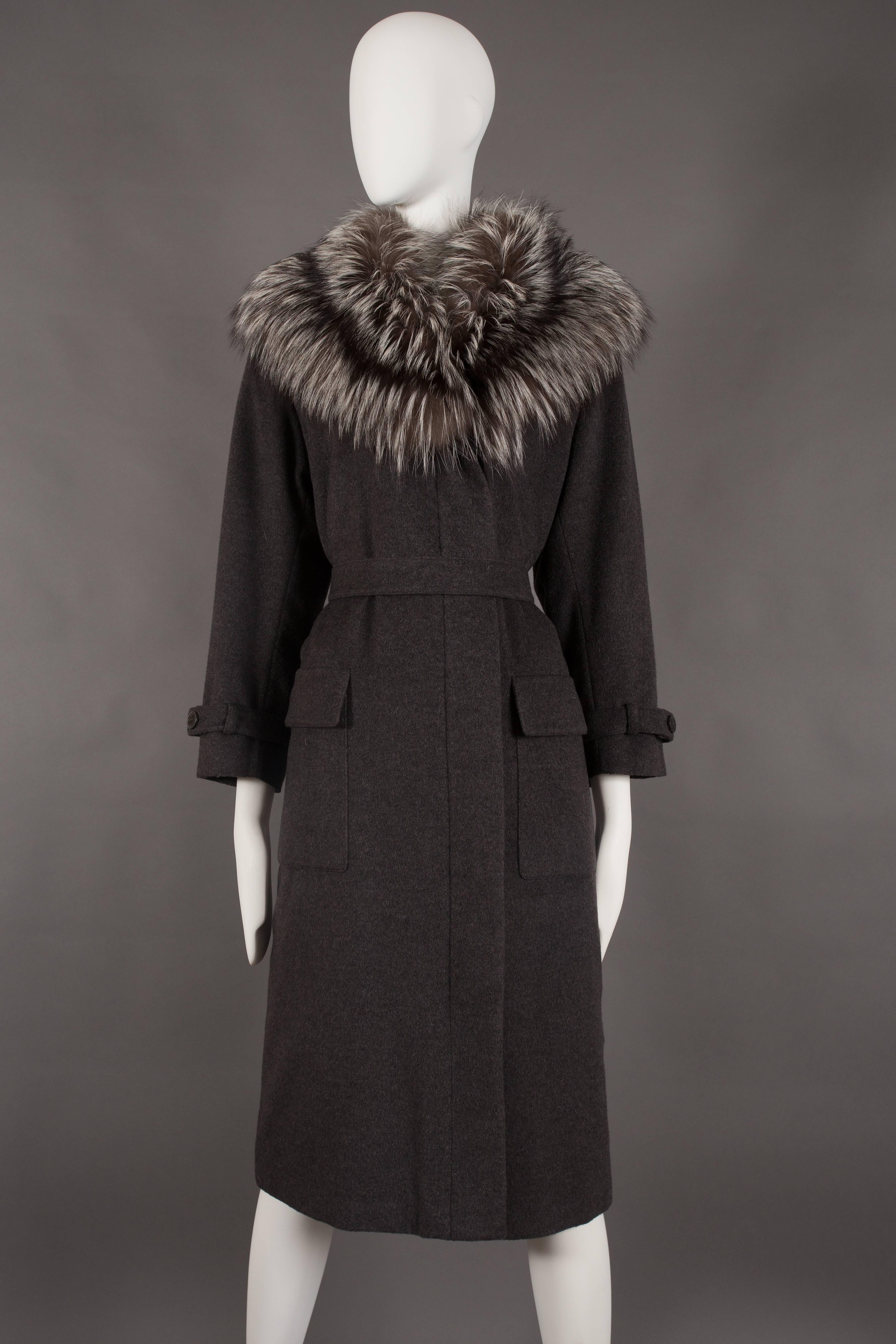 A Yves Saint Laurent charcoal grey cashmere fall coat, circa 1990. 

Exaggerated arctic fox fur collar, hidden button closures on front opening, matching double button belt, two front flap pockets and black satin quilted lining. 