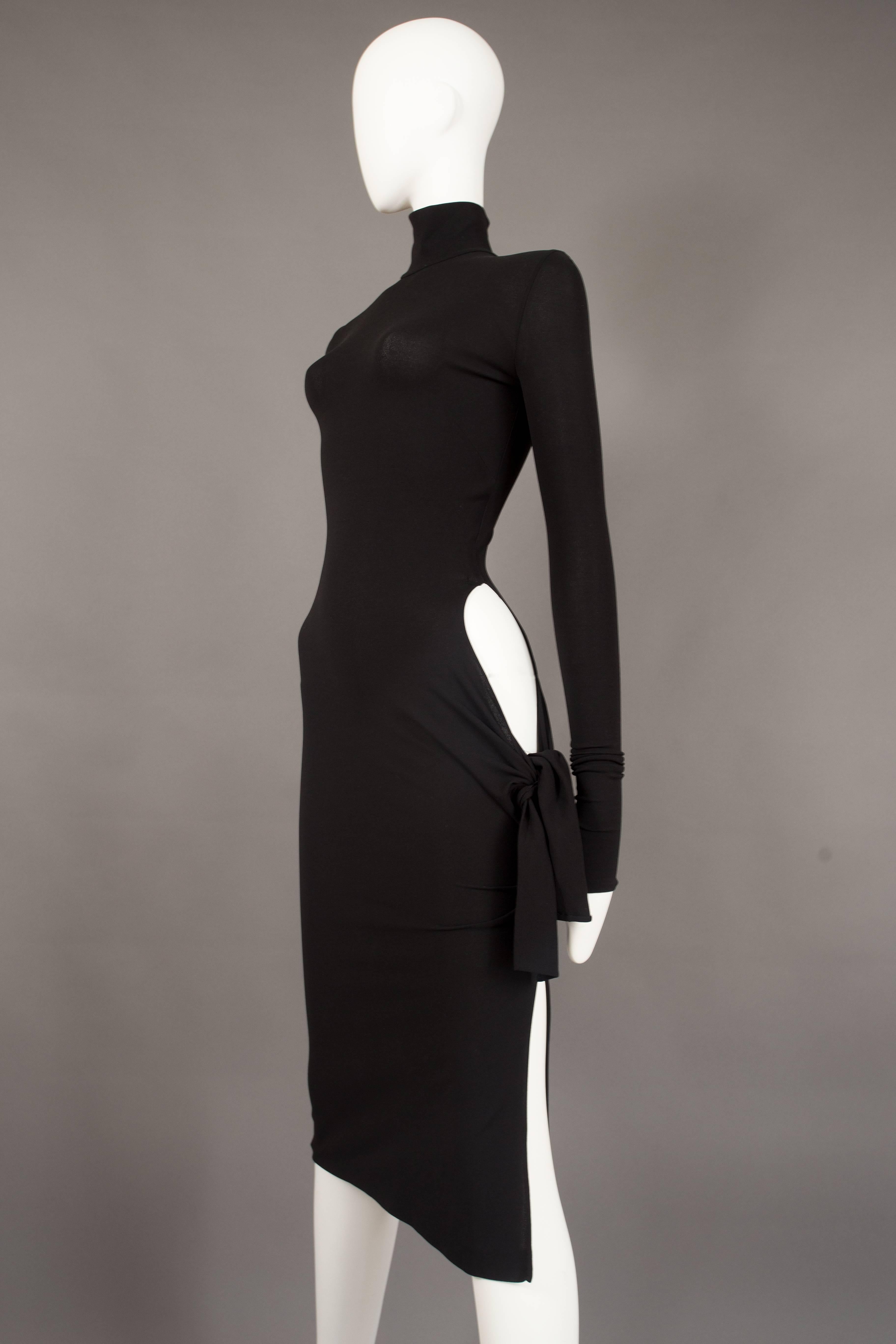 An iconic and rare Dolce & Gabbana bodycon evening dress from the spring summer 2001 collection. Black spandex-like stretch fabric, turtleneck, long fitted sleeves, invisible zip closure, high leg slit and circular cut on the lower hip with tie-up