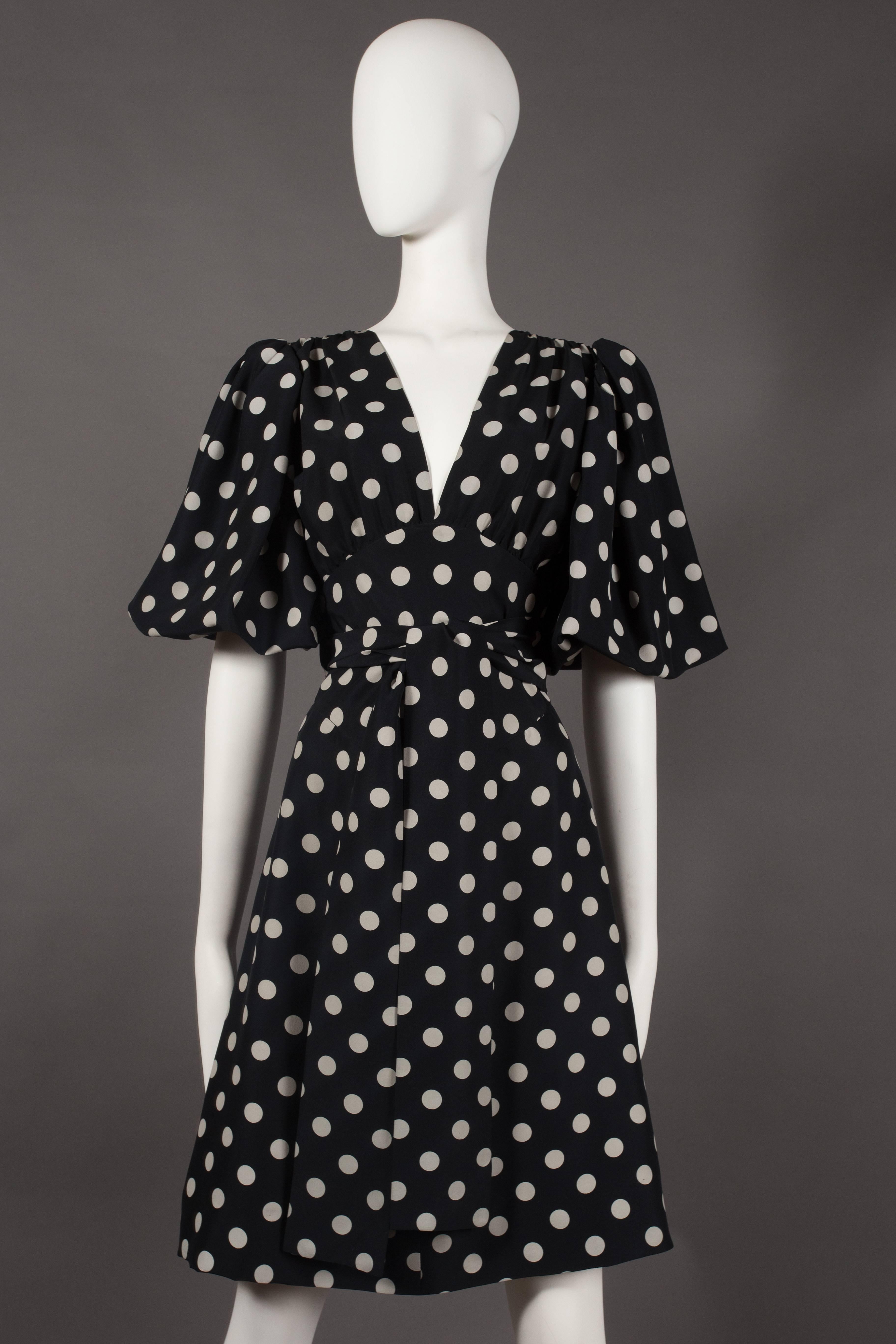 A Yves Saint Laurent polka dot silk wrap dress, circa 1970s. The dress features a low v-neck, pleated puff sleeves, wrap belt closure on waist and button closures at the rear of the dress.