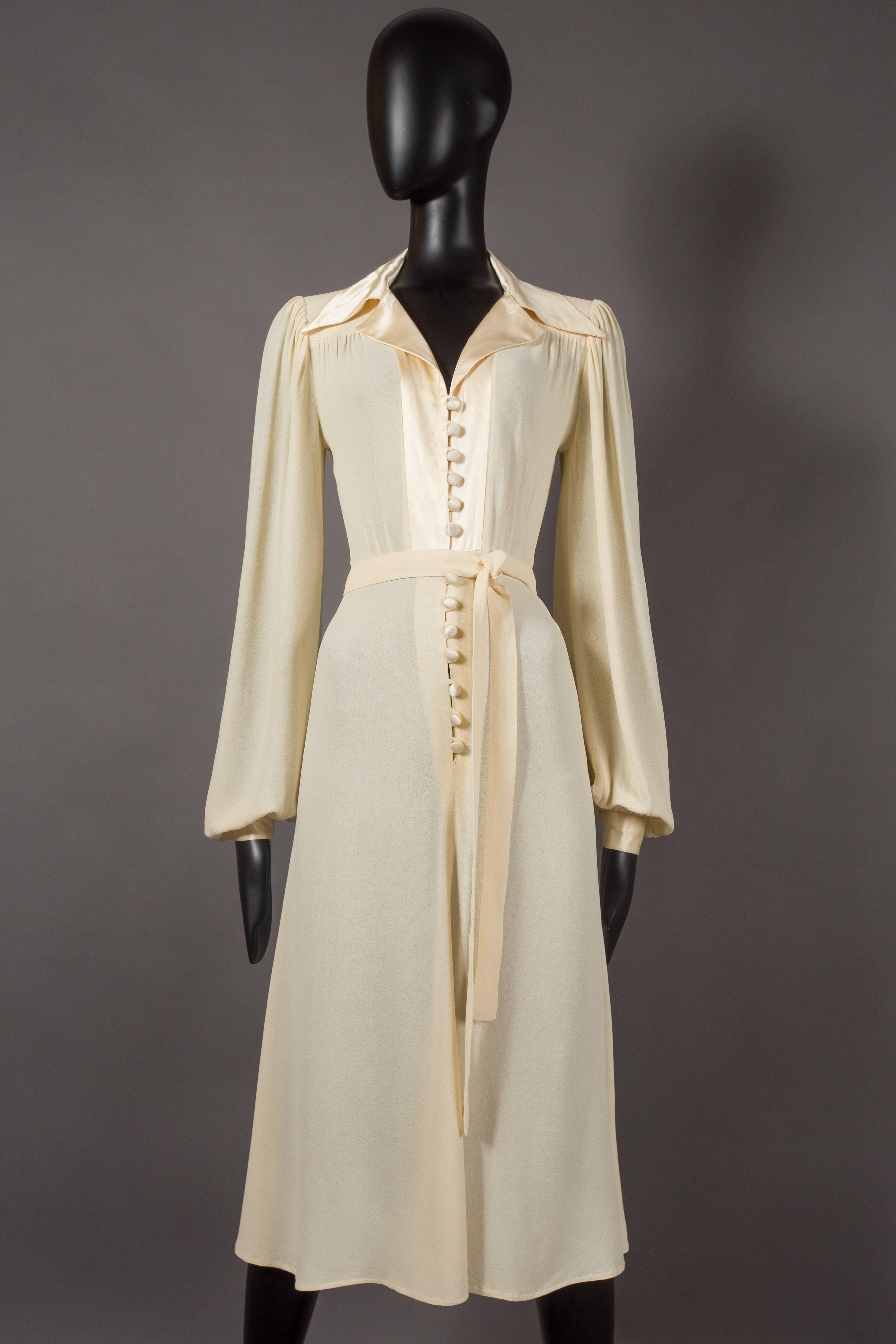 An Ossie Clark for Radley ivory moss crepe evening dress, circa 1974. Satin trim, cuff and button closures, waist belt and pleated bishop sleeves. An iconic dress by an equally iconic fashion designer, this dress will never go out of style! 