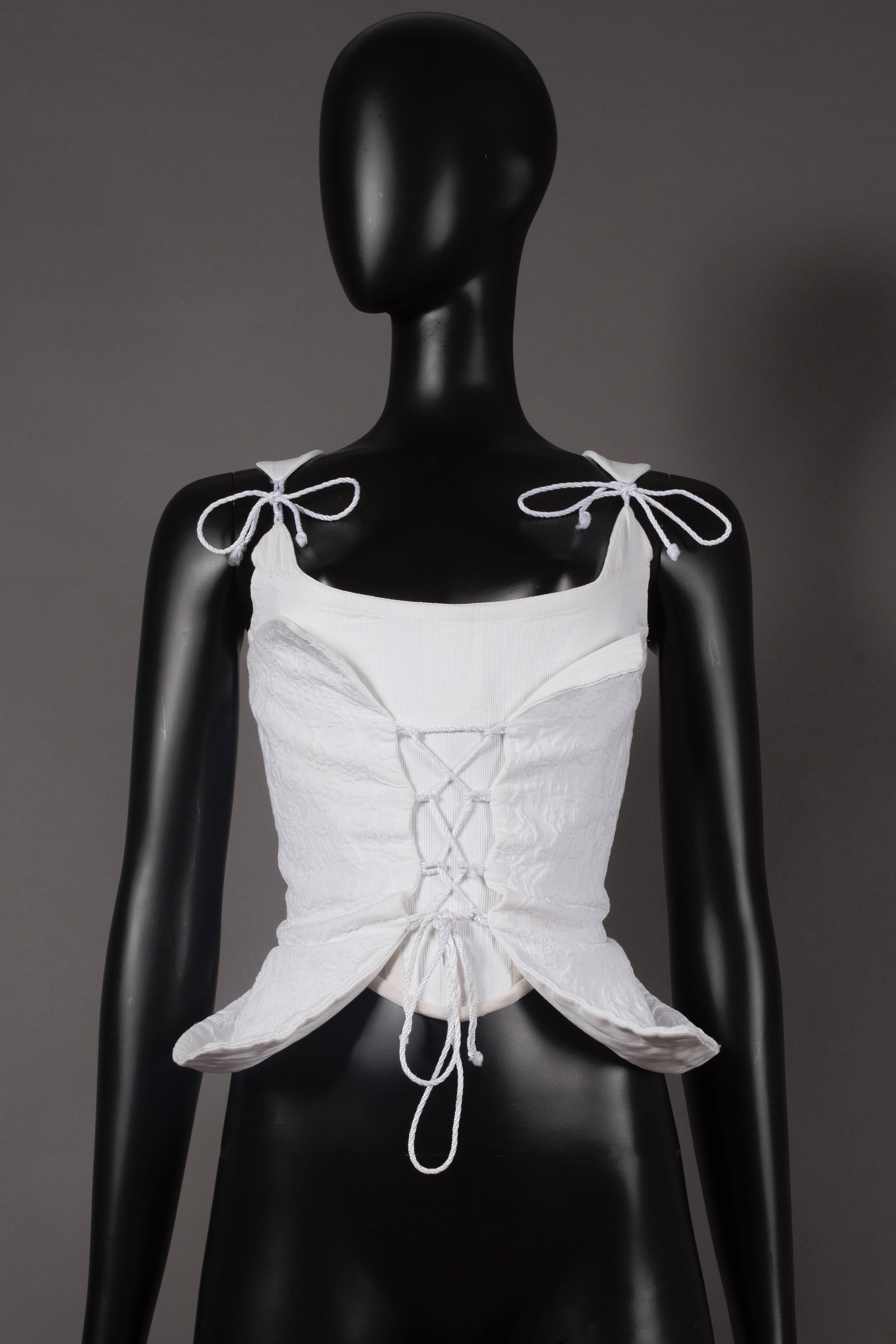 A rare 18th century inspired Vivienne Westwood wedding corset, circa 1995. White cotton piqué bodice laced across boned corset of ribbed white cotton, side panels of white mesh, lace string fastens shoulder straps at front and zip closure at the