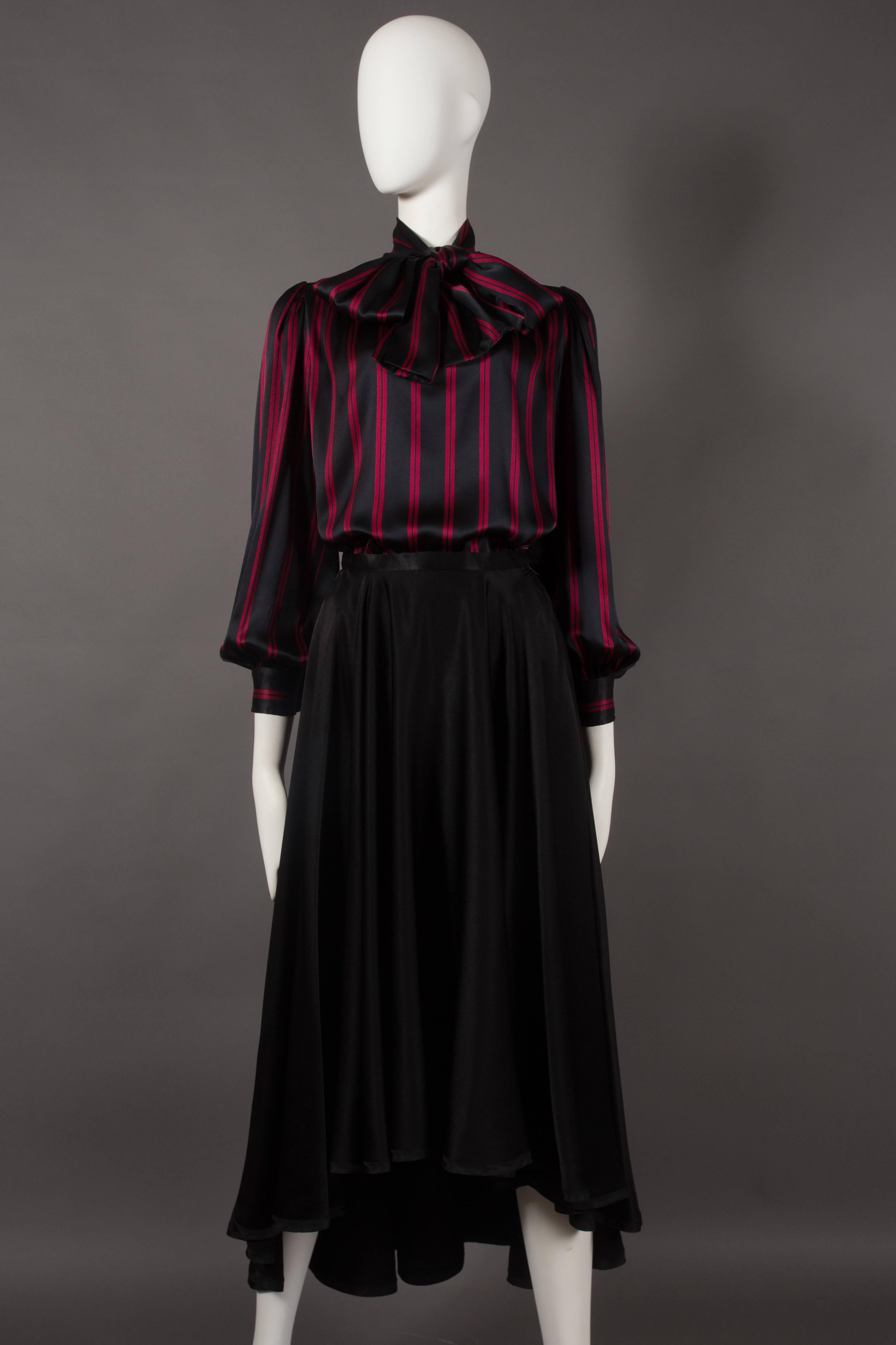 A Yves Saint Laurent silk evening ensemble, circa 1970s. Black striped blouse with bishop sleeves and pussy bow neck tie. High waisted black skirt with high front and low black. 