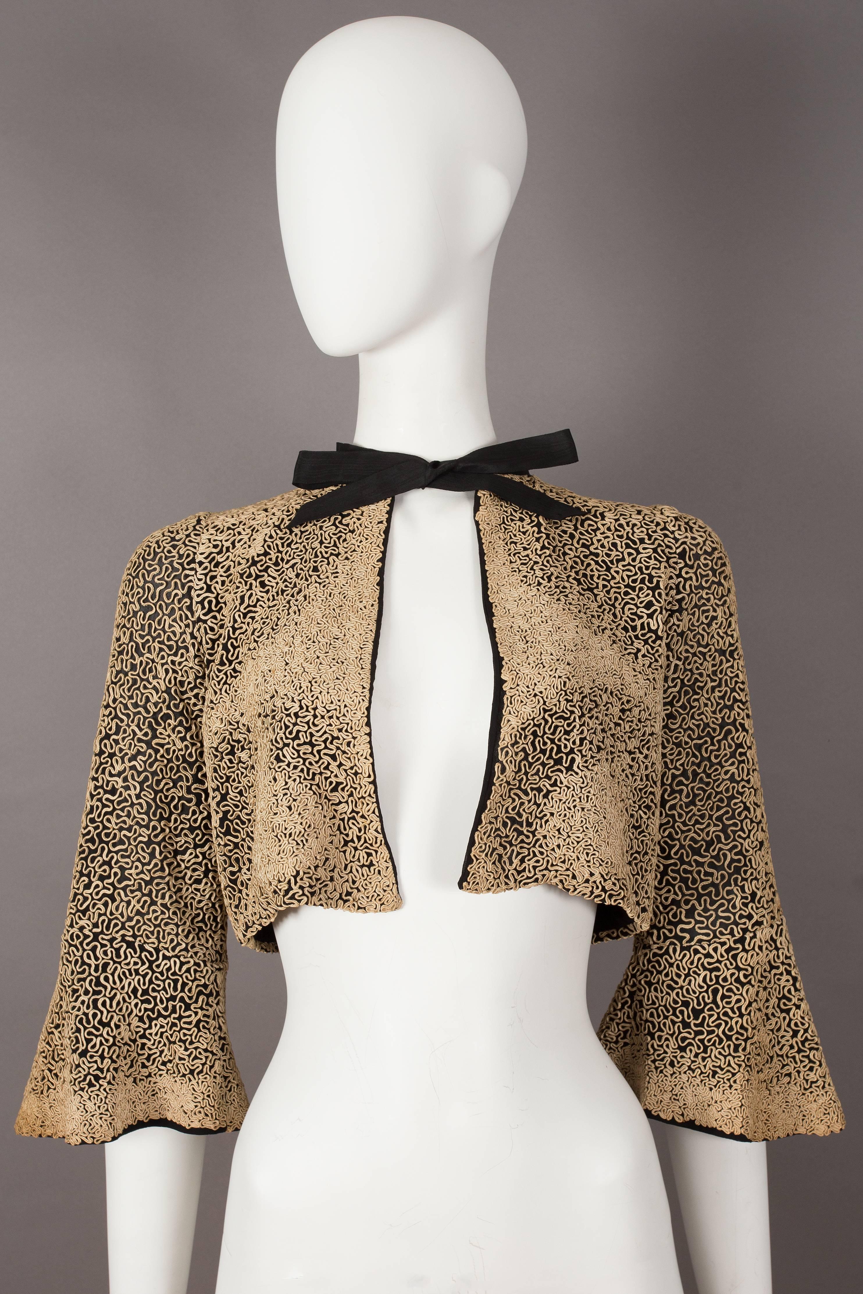 A beautiful 1930s bolero evening jacket with intricate ribbon embroidery throughout, cropped bell sleeves, silk chiffon lining and black bow fastening on the collar.