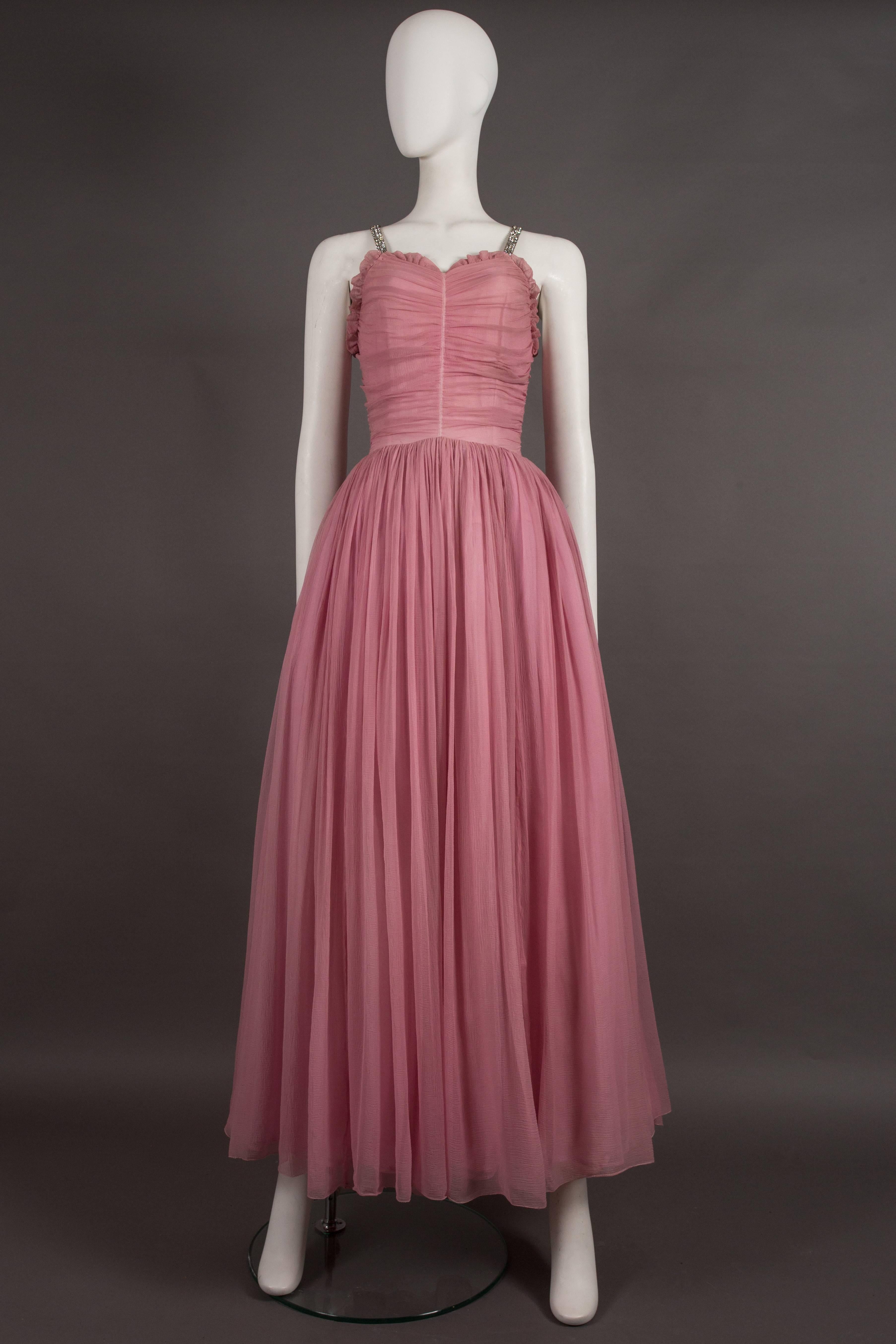 An exceptional couture 1940s evening gown in baby pink silk chiffon. The dress features rhinestone should straps, ruffled trim, ruched bust with original metal zipper and full pleated skirt with three interior layers of tulle, voile and silk