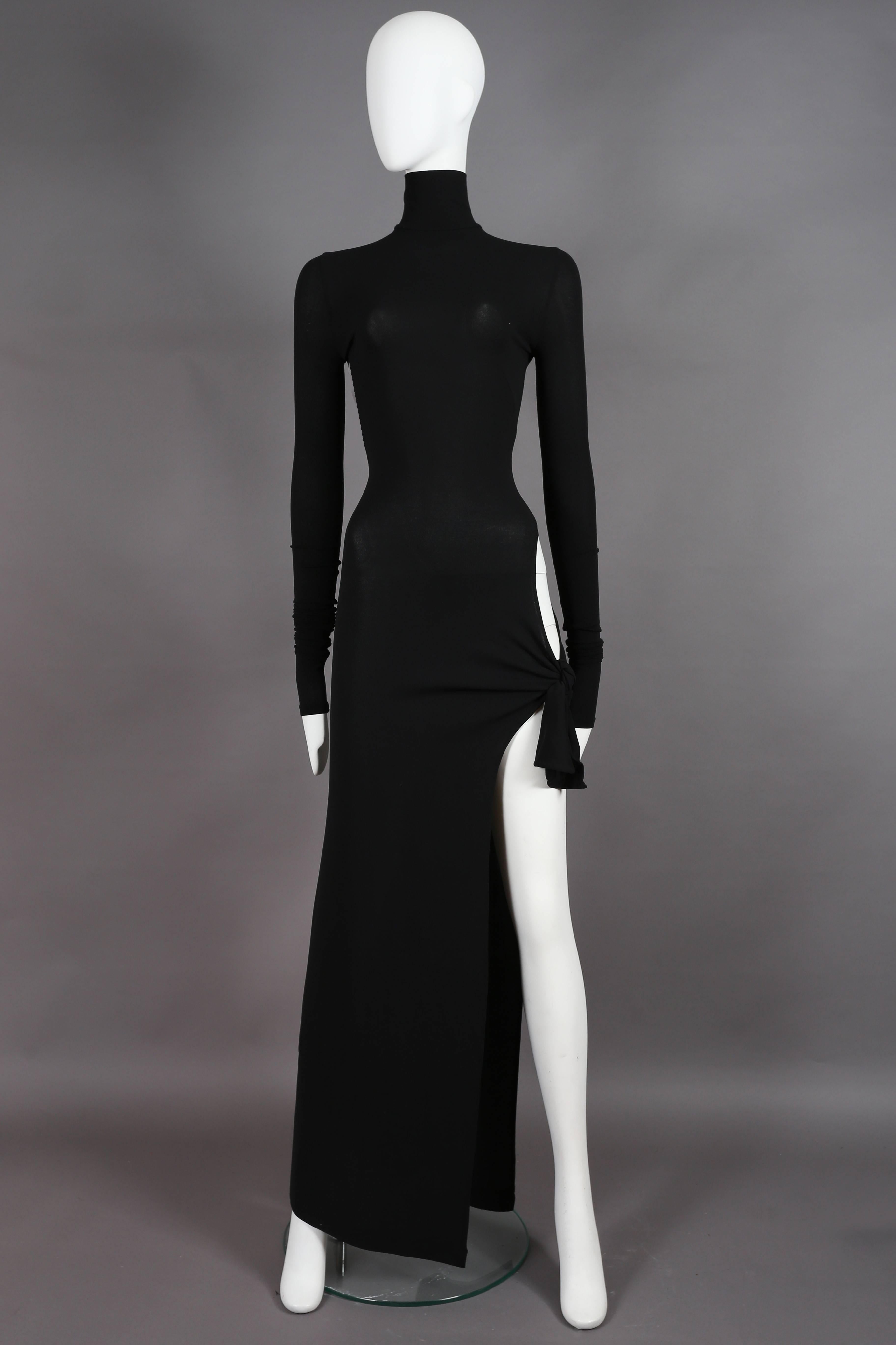 An iconic and rare Dolce & Gabbana bodycon evening dress from the spring summer 2001 collection. Black spandex-like stretch fabric, turtleneck, long fitted sleeves, invisible zip closure, high leg slit and circular cut on the lower hip with tie-up