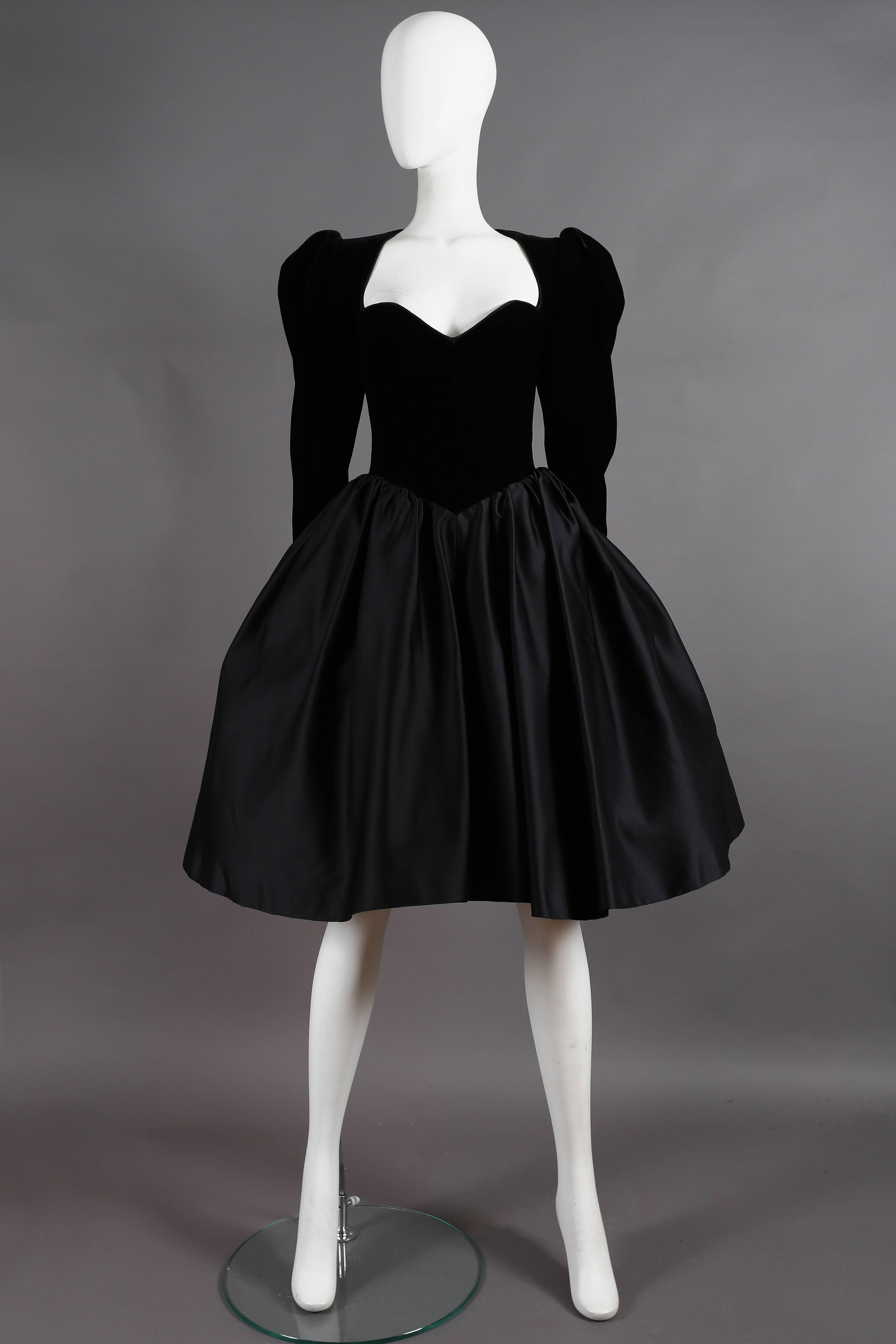 An exquisite Yves Saint Laurent Haute Couture cocktail dress, autumn-winter 1981. The dress features a low-cut black velvet bodice with a braided trim, puff shoulders, and metal zip fastenings. The skirt is pleated from the synched in waist with
