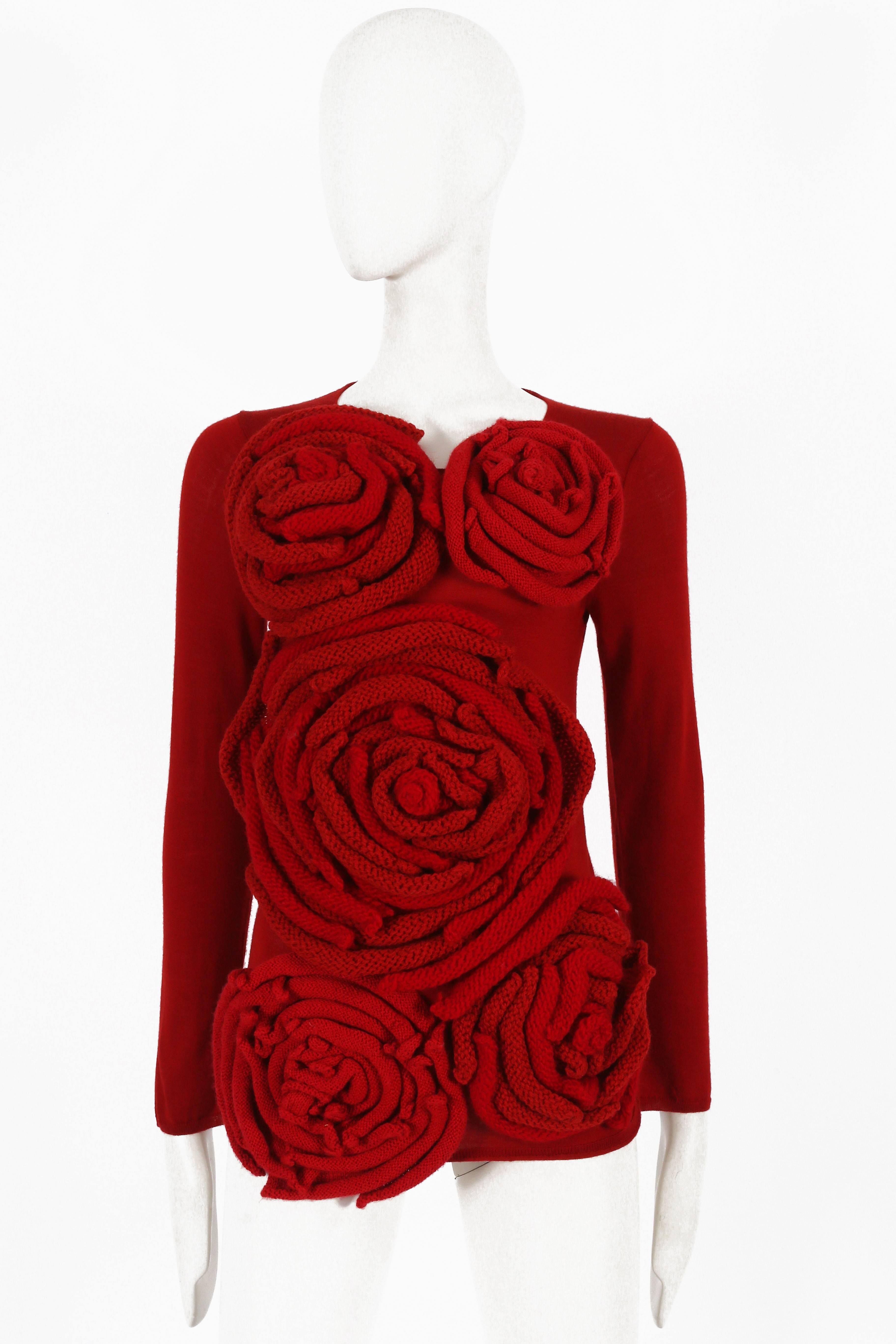 Presenting a striking Comme des Garçons red knitted sweater adorned with large knit appliques resembling roses, a standout piece from the 2014 collection. This sweater showcases the brand's distinctive and artistic approach to knitwear.

The rich
