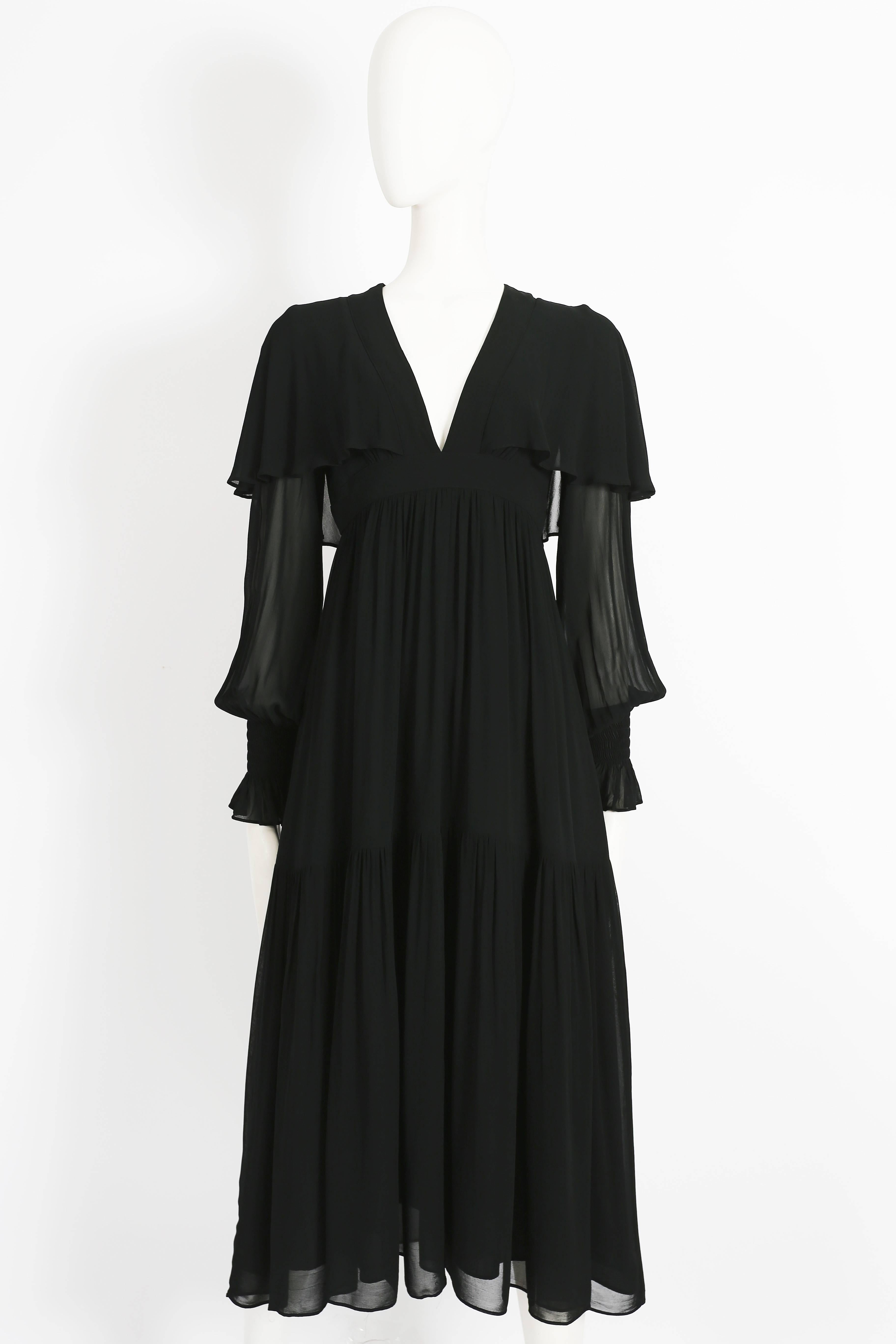 Ossie Clark black evening dress constructed in chiffon crepe with satin lining, circa 1972. The dress features attached capelet, pleated tiered design, shirred elasticated cuffs and zip fastening. 