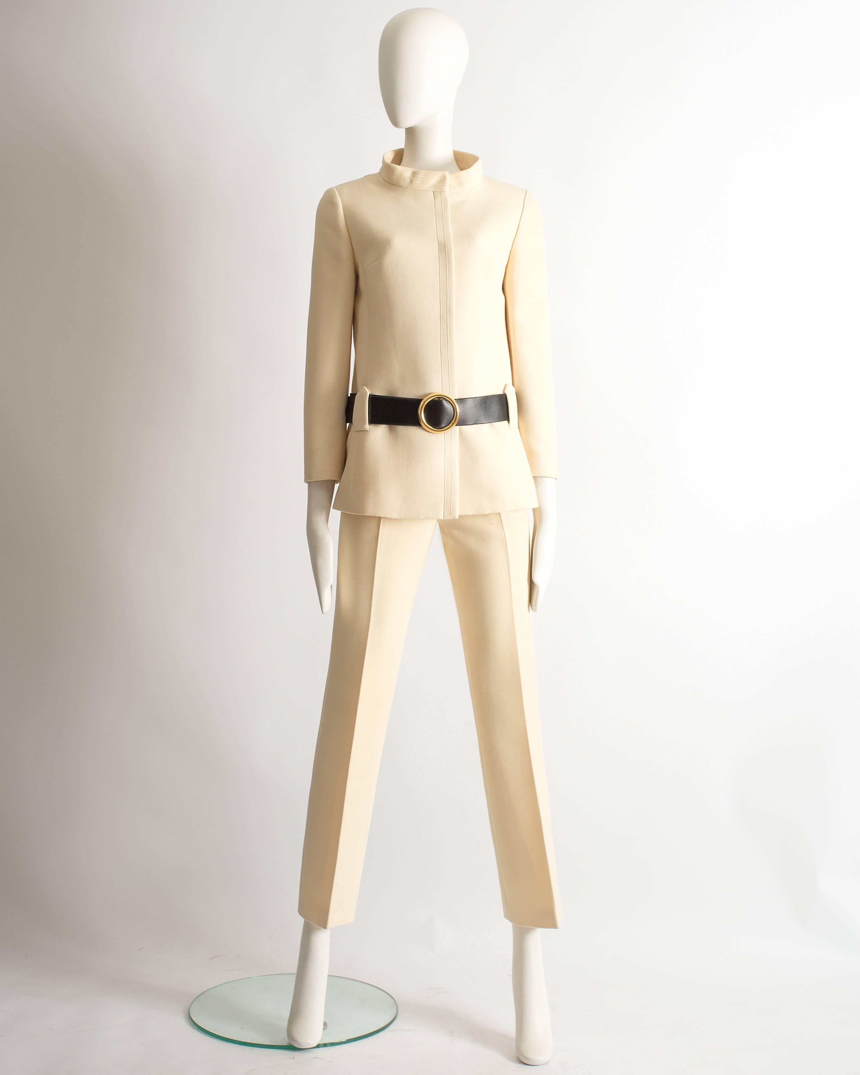 Pierre Cardin ivory wool pant suit, circa 1968. Tailored jacket with high standing collar, snap button closures, wide black faux leather belt with large gold metal buckle. High waist, slightly flared cropped pants with zip fastening. 

