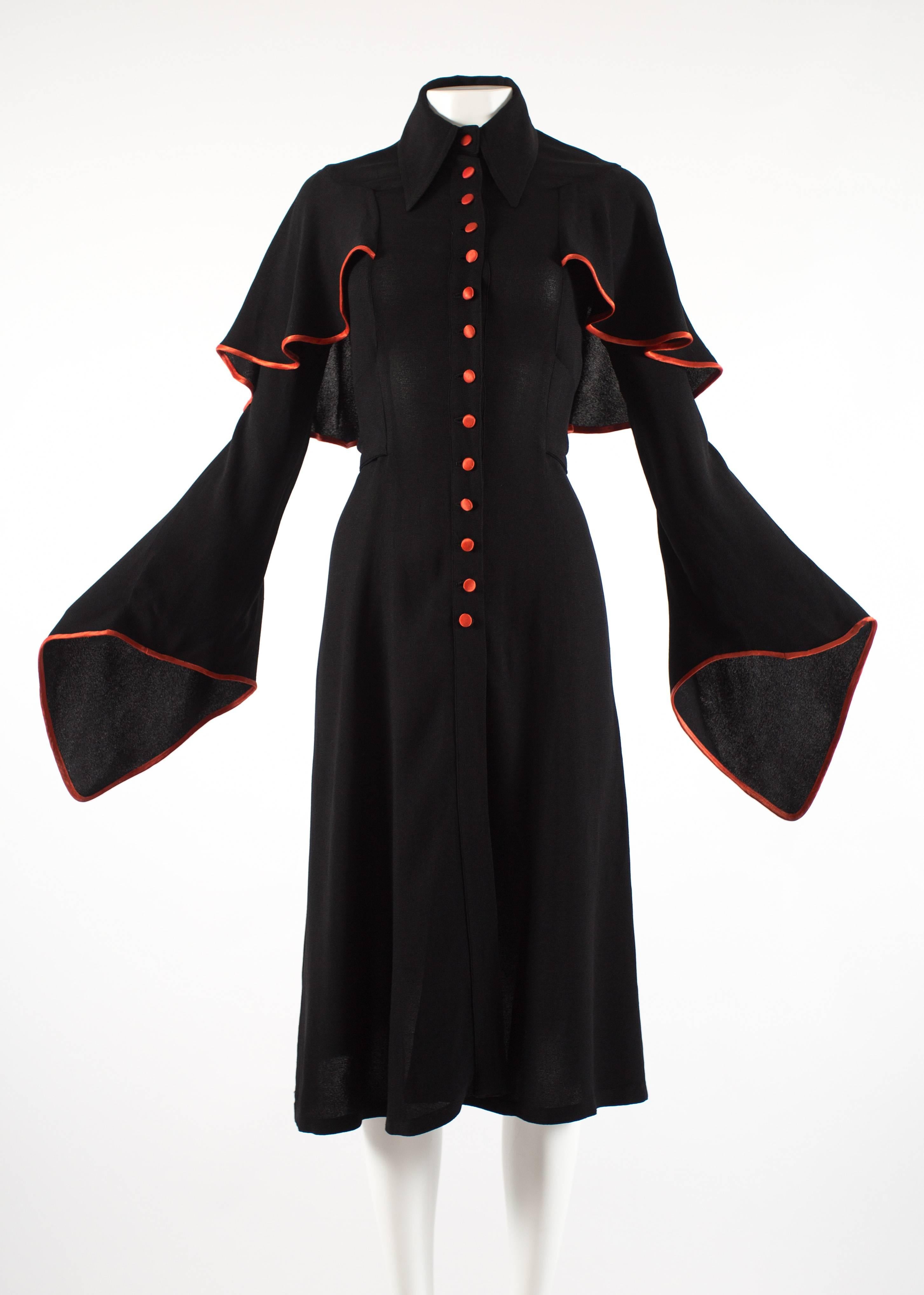 Ossie Clark 1970 black moss crepe mid length dress with red satin trim, button fastenings, pointed collar, attached waist belt and exaggerated bell sleeves.
