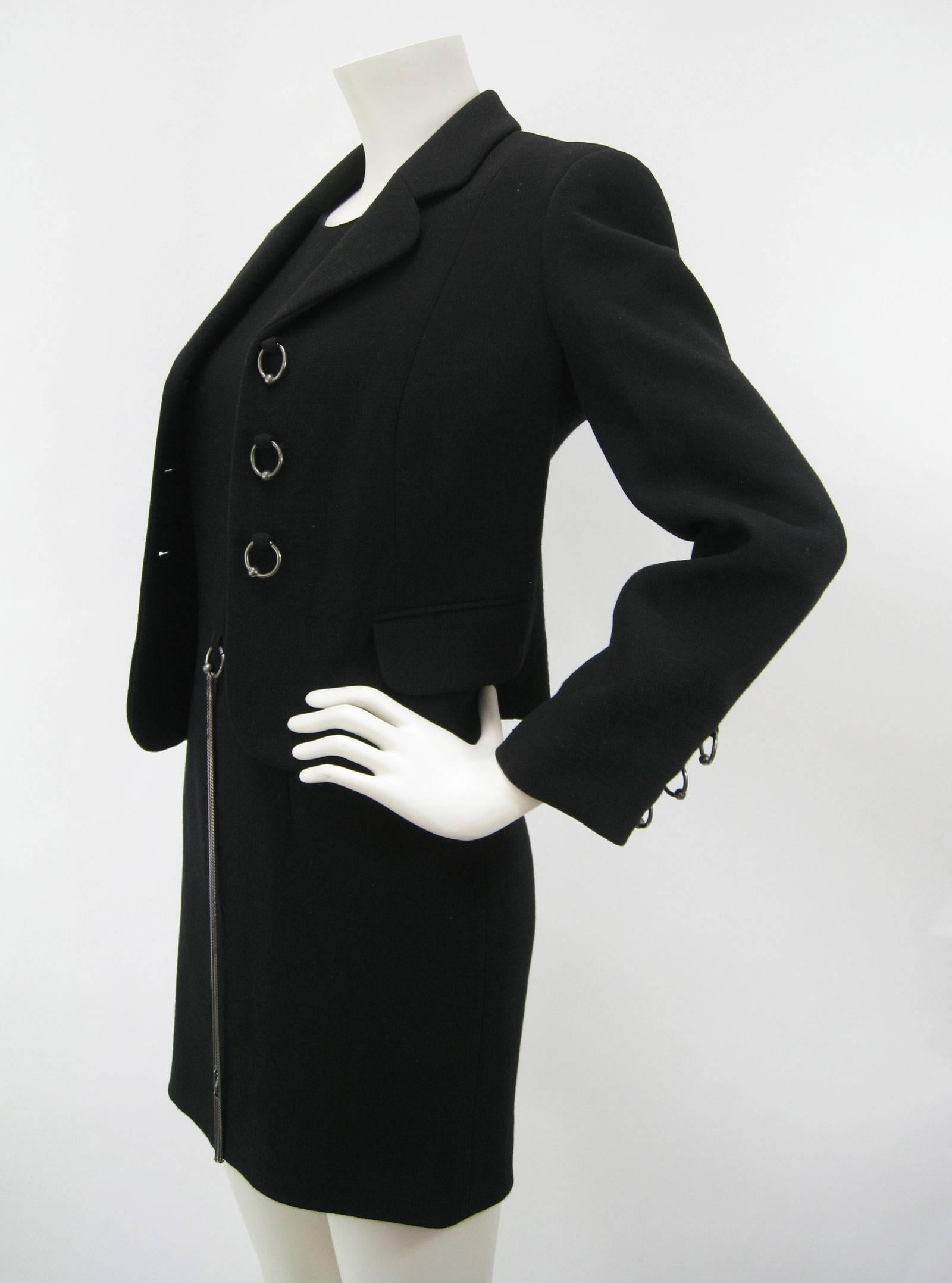Vintage Moschino black dress and jacket suit.
Minimal black sleeveless dress with attached silver chain belt.
Back zipper. Fully lined.
Jacket hits at hip and features ring "buttons" (jacket unbuttoned in pics)
Front flap