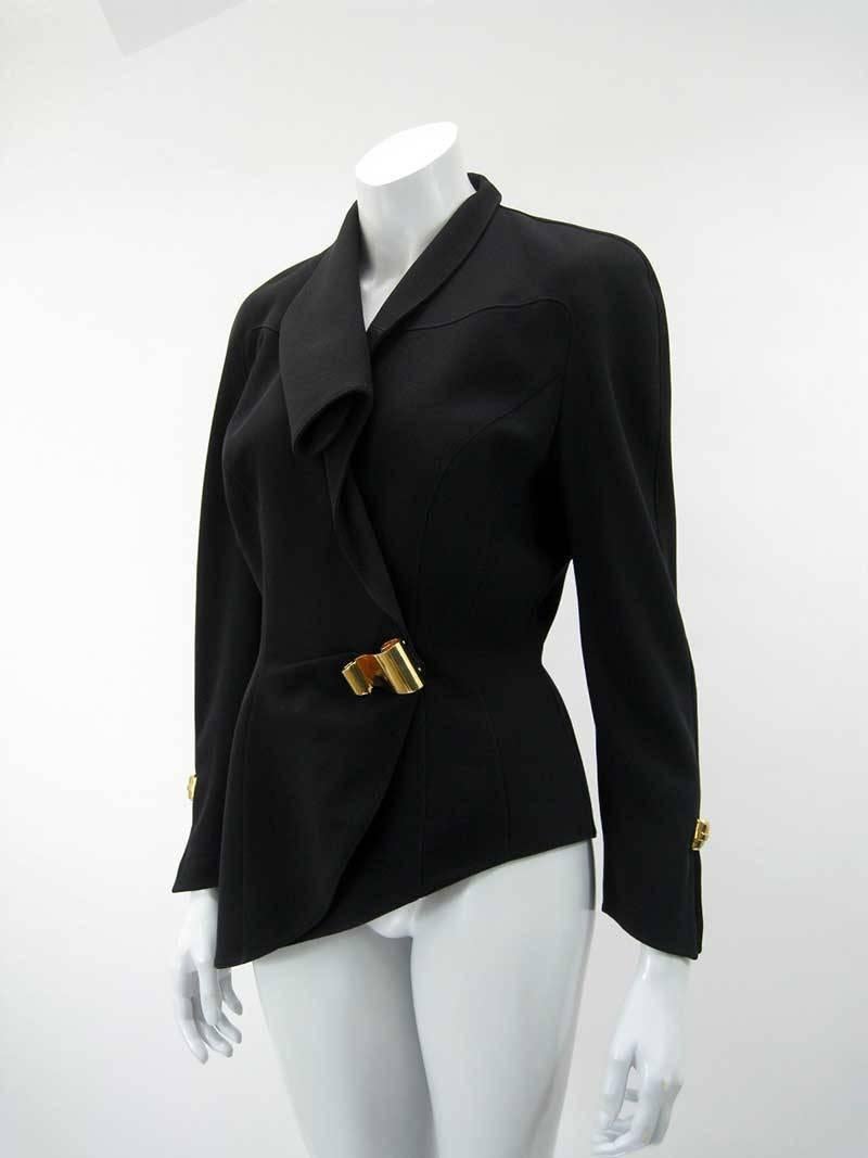 Stunning Thierry Mugler black asymmetrical blazer.

Fold over collar. Longer fitted shape with exaggerated shoulders.

Hidden snap closures with bright brass decorative scroll embellishments on front side and wrists.

Tagged size 38.

Fully lined.
