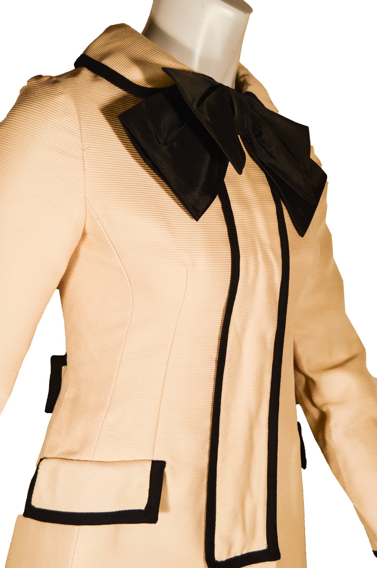 This adorable Mod-era coat in cream has contrast black piping and buttons. There are two faux pockets and an oversized black silk organza bow at the neck. There is a hidden zipper front behind the center placket. The coat is a size small.