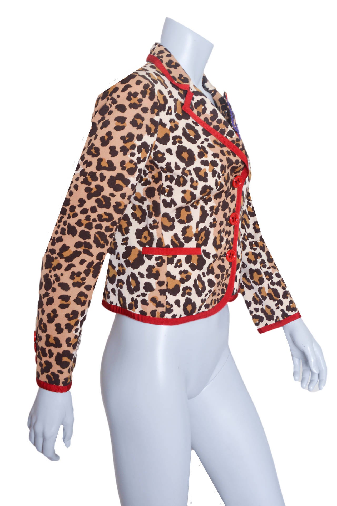 Whimsical Moschino Cheap and Chic cropped leopard print jacket.
Fitted shape.
Left lapel is embellished with kitty pin.
Pin features rick rack, buttons and sequins.
Jacket has red ribbon trim and three button closure.
Faux pockets.
Lined.