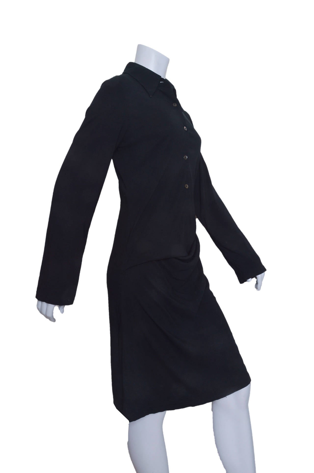 Black Ann Demeulemeester shirt dress.
Asymmetrical gathering at hip.
Gathered into a pouch.
Four button closures with golf over collar.
Long straight sleeve.
Unlined.
Tagged a size 38.