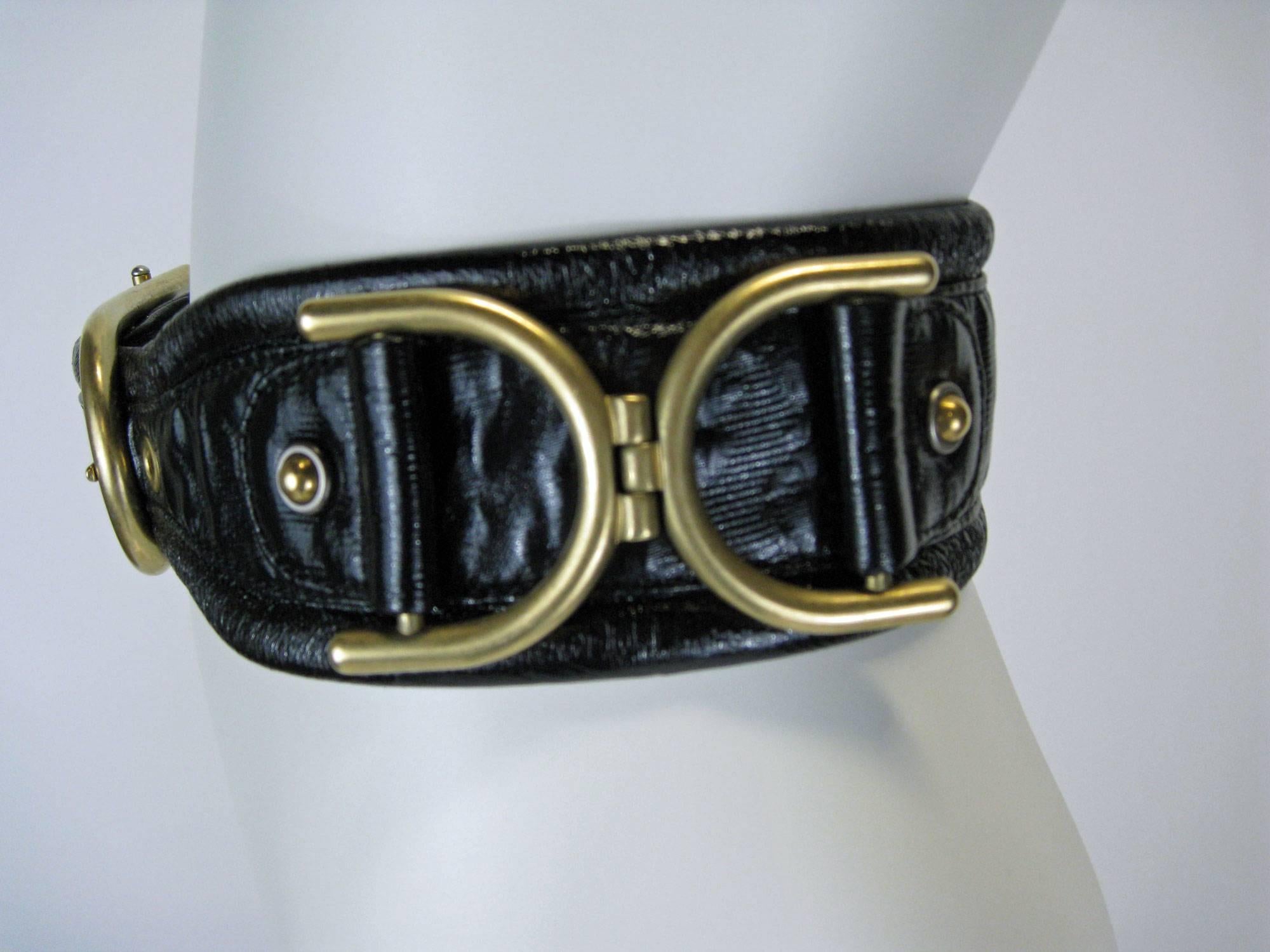 Substantial Stella McCartney leather cinch belt.
Shiny black, not quite patent leather with embossed texture.
Large brass horseshoe buckle with brass grommeted holes.
Double horseshoe hardware on sides with studs.
Tag reads size