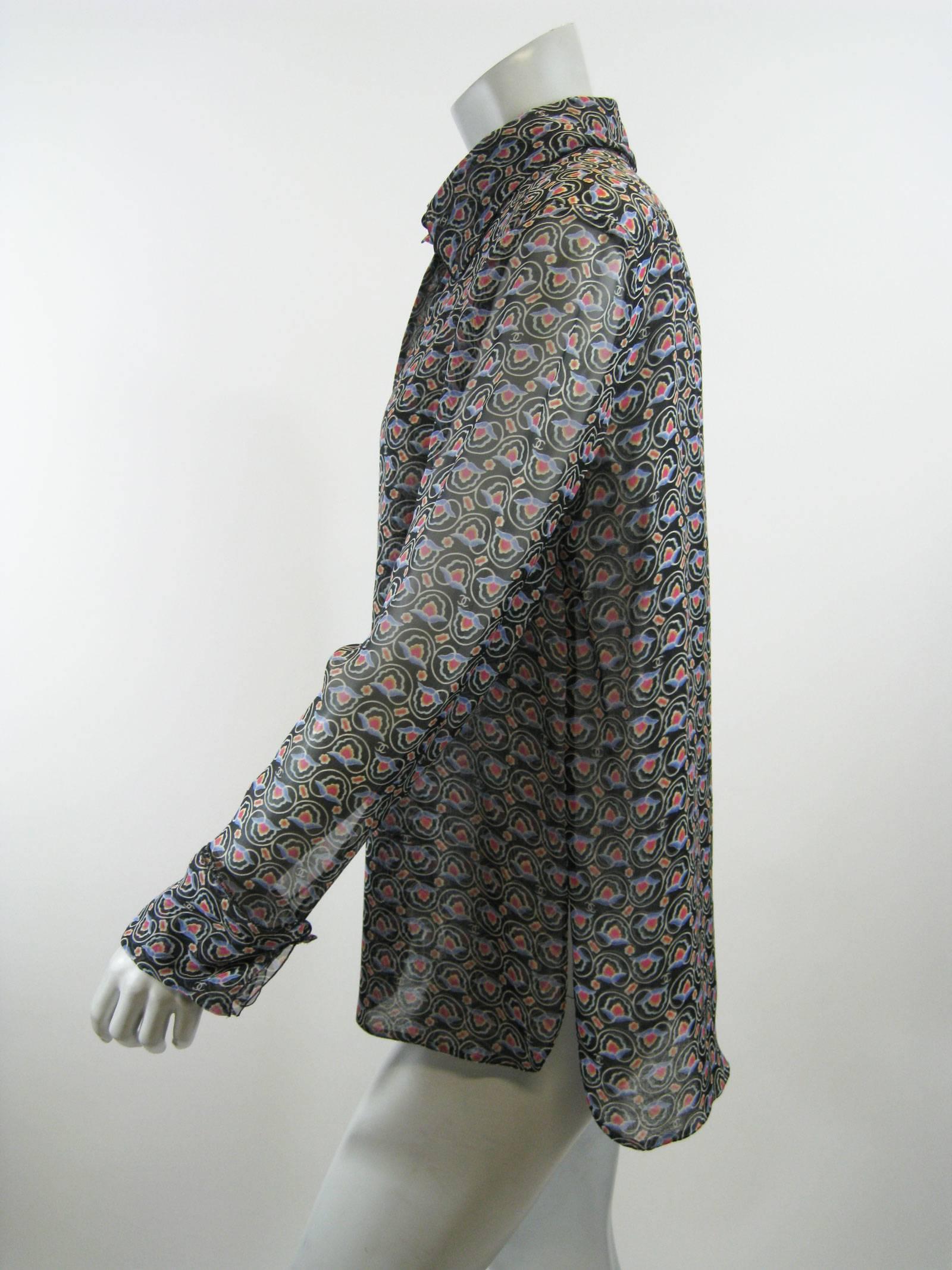 Light and sheer Chanel blouse.
Black white white, pink, gold and blue floral motof with Cc logo,
Hidden button placket.
Small black plastic Chanel imprinted buttons. 
Fold over cuffs with buttons.
Fold over collar, 
There are two button holes