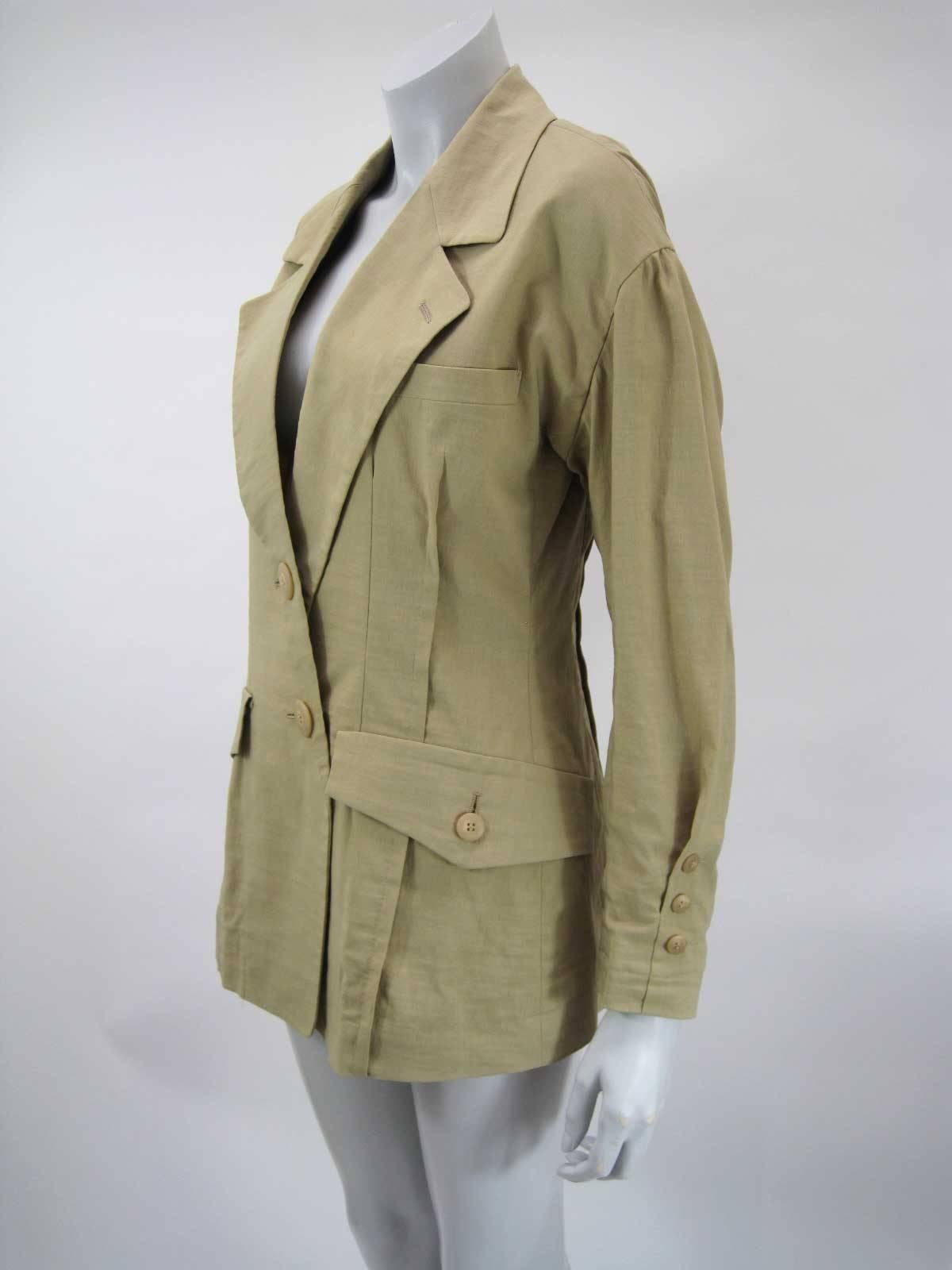 Vintage Issey Miyake menswear inspired blazer.

Tan khaki color.

Exaggerated shoulders with slightly puffed sleeves.

Long fitted shape. 

Pintuck pleats and slightly asymmetrical button closure.

Double asymmetrical wrap around buttons.

Button
