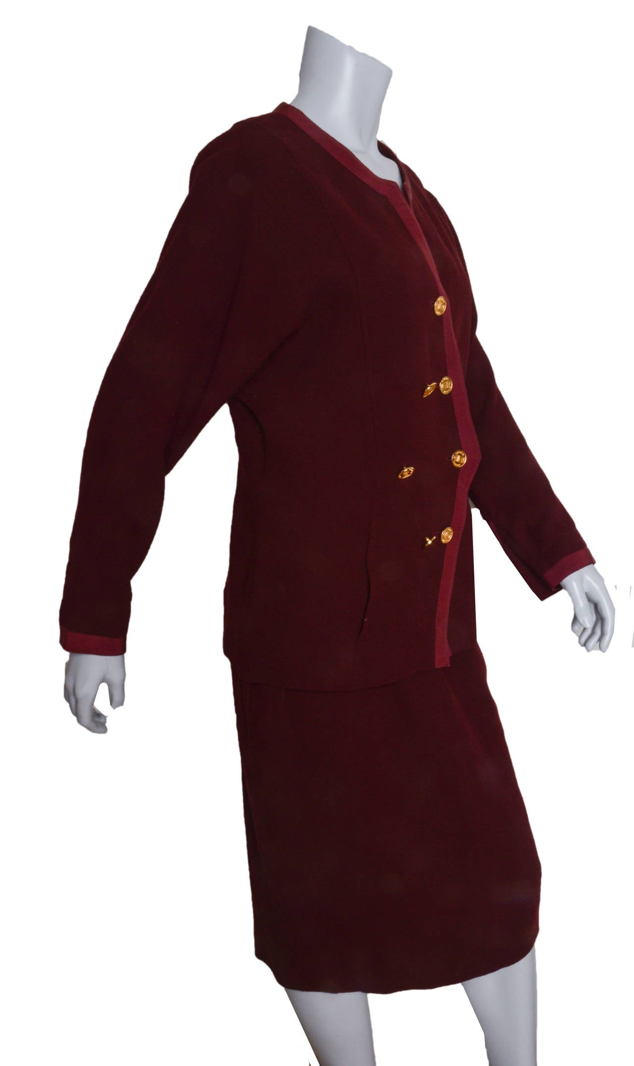 Vintage Chanel Boutique burgundy knit skirt suit.
Wool/nylon blend.
Double breasted jacket features contrasting ribbon trim.
Gold coin-like embossed Chanel buttons adorn the front in a diamond shape.
Gold buttons at cuff.
Lined.

Measurements:
Bust:
