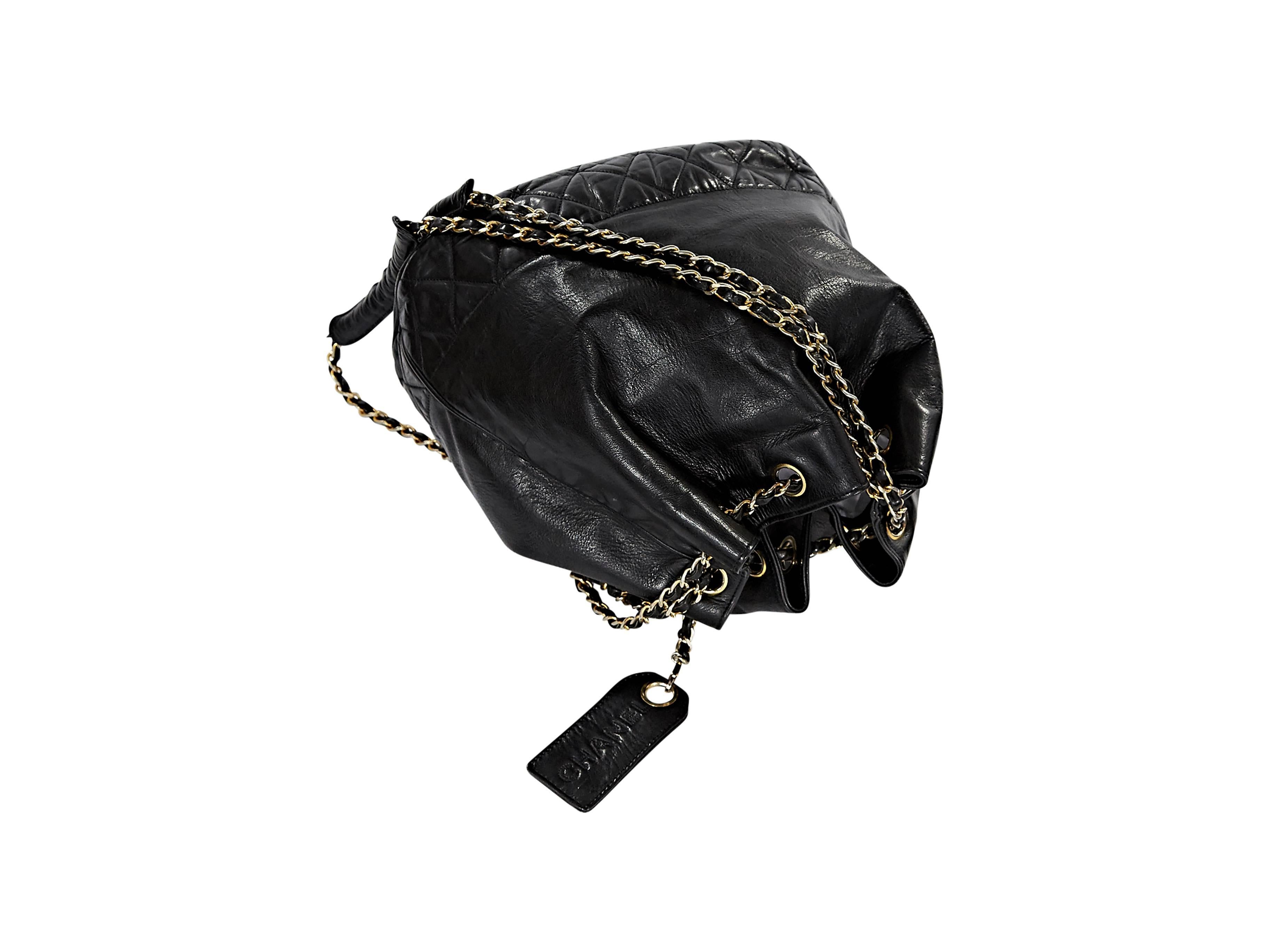 Black leather bucket bag by Chanel.  Double woven leather chain straps.  Drawstring closure.  Hanging embossed logo tag.  Quilted trimmed bottom.  Goldtone hardware.  