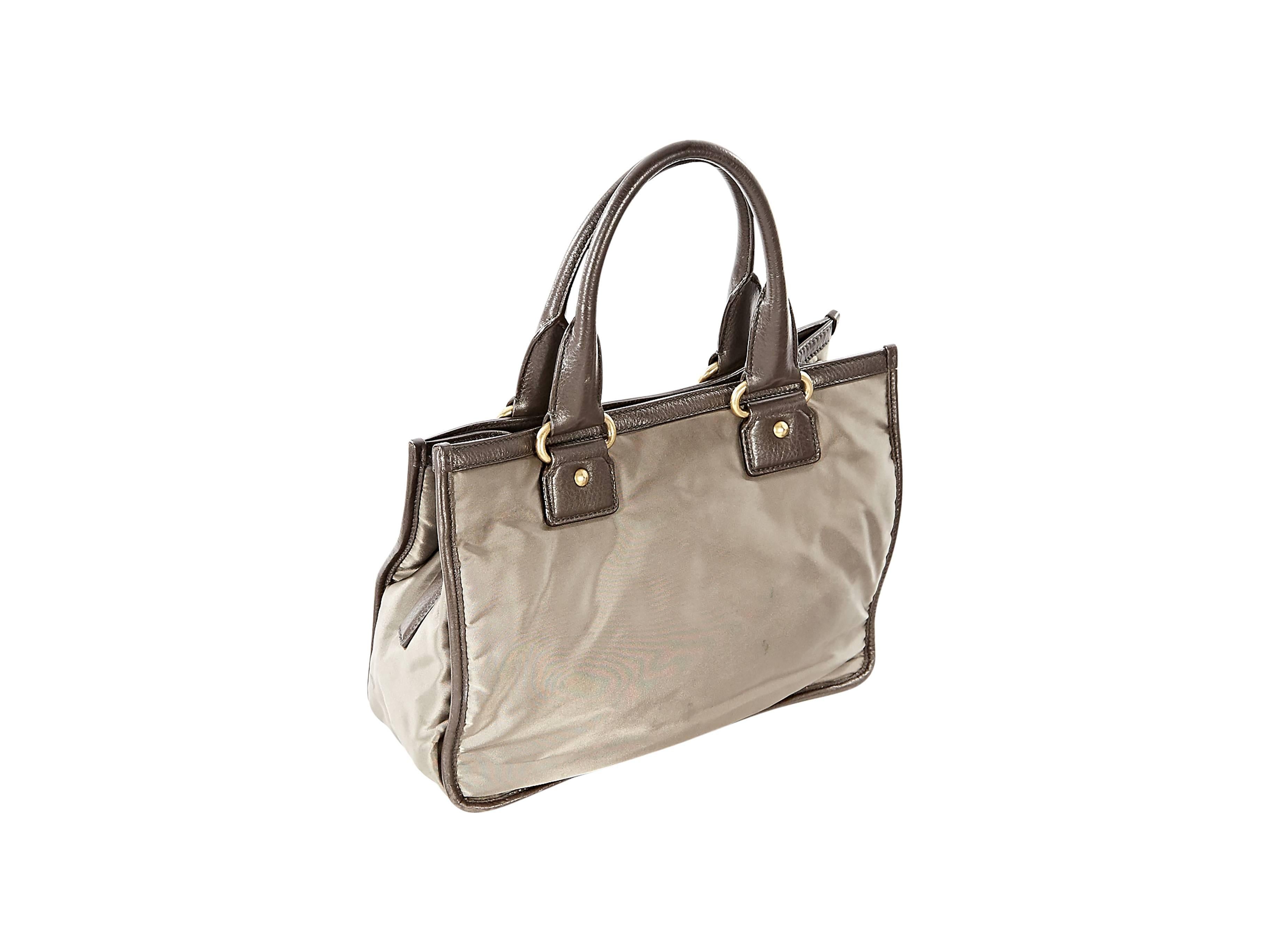 Taupe fabric tote bag by Prada.  Logo design accents front.  Trimmed with brown leather.  Tote carry handles.  Snap tab closure.  Lined interior with zip pockets.  Protective metal feet.  Goldtone hardware.  13