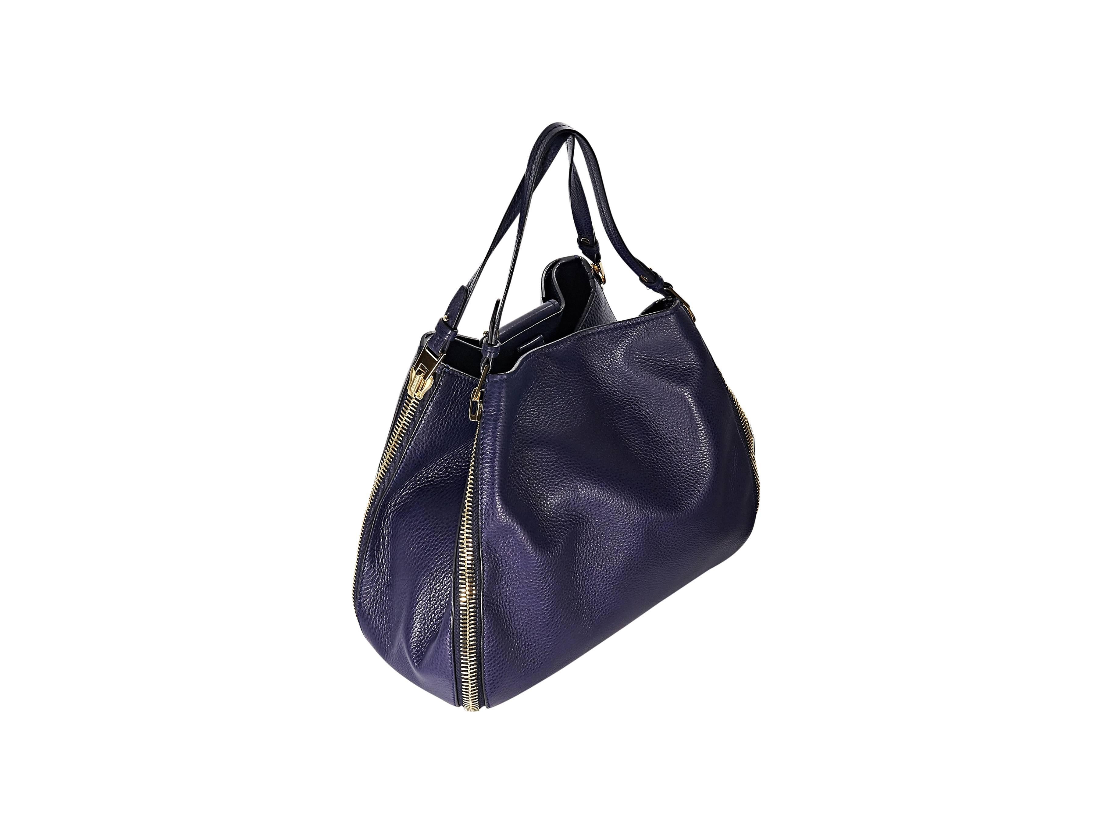 Product details: Navy pebbled leather Sedgwick tote bag by Tom Ford. Double shoulder straps. Magnetic snap and clip bridge closure. Side zippers. Lined interior with inner zip and slide pockets. Protective metal feet. Goldtone hardware. Dust bag