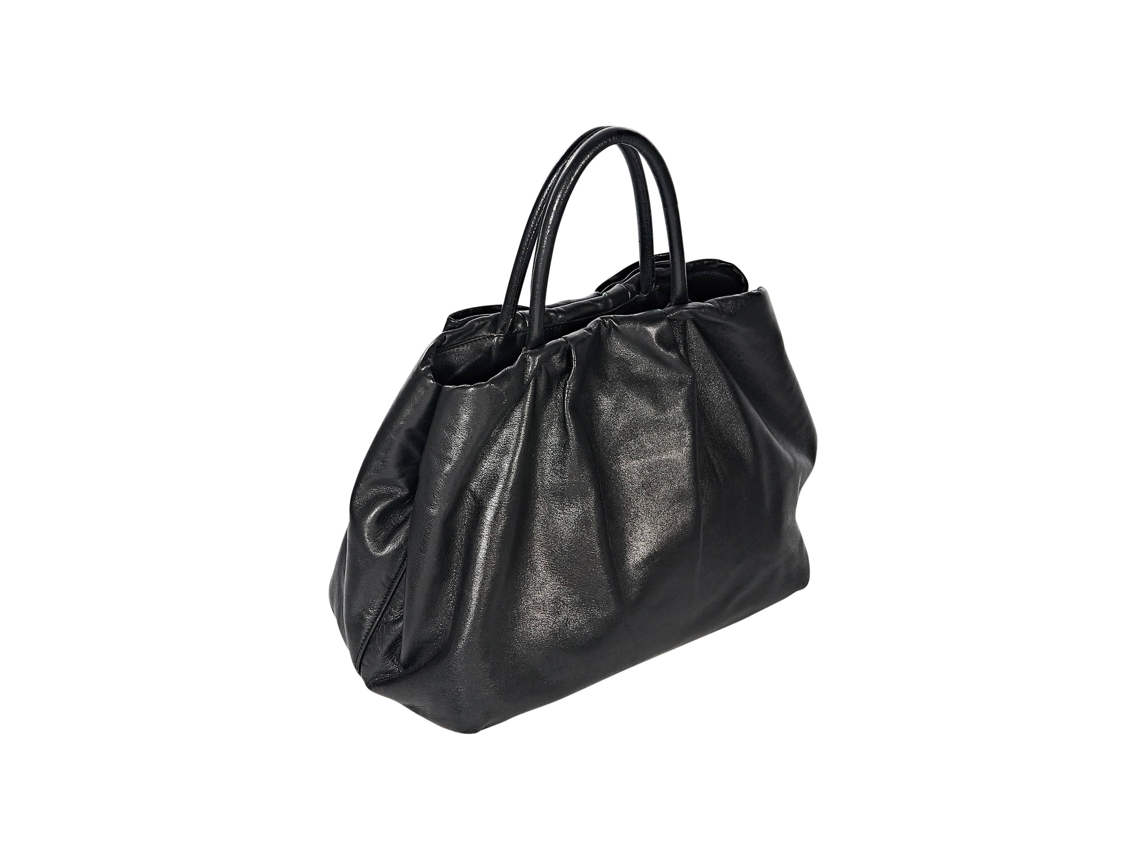 Product details: Black nappa leather tote bag by Prada. Bow accents front. Dual carry handles. Side snaps. Magnetic snap closure. Lined interior with inner zip pockets. Protective metal feet. Goldtone hardware. 11