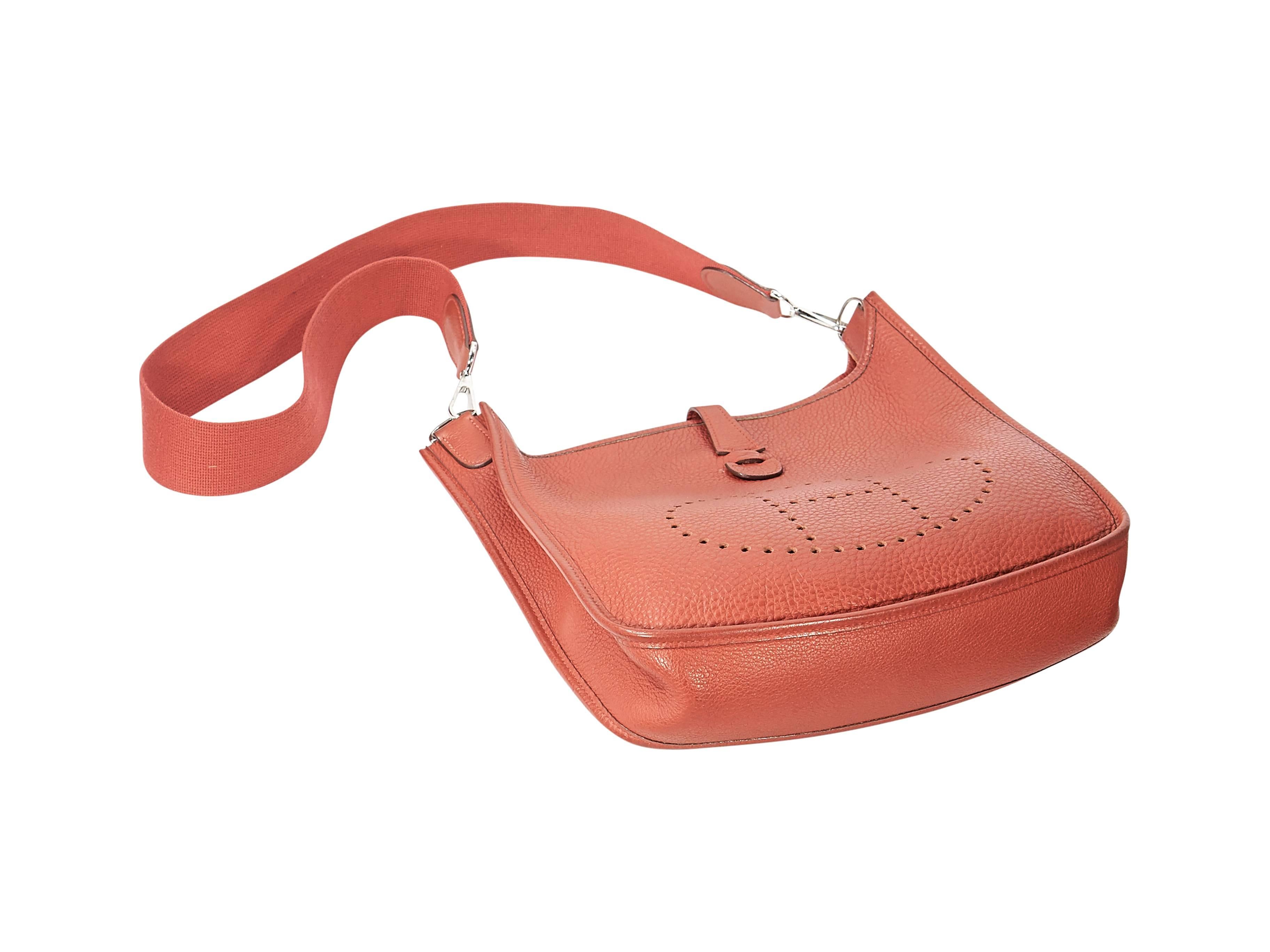 Product details: Red pebbled leather Evelyne III PM bag by Hermes. Perforated front logo design. Detachable shoulder strap. Top tab closure. Lined interior with inner slide pocket. Palladium-plated hardware. 11.3