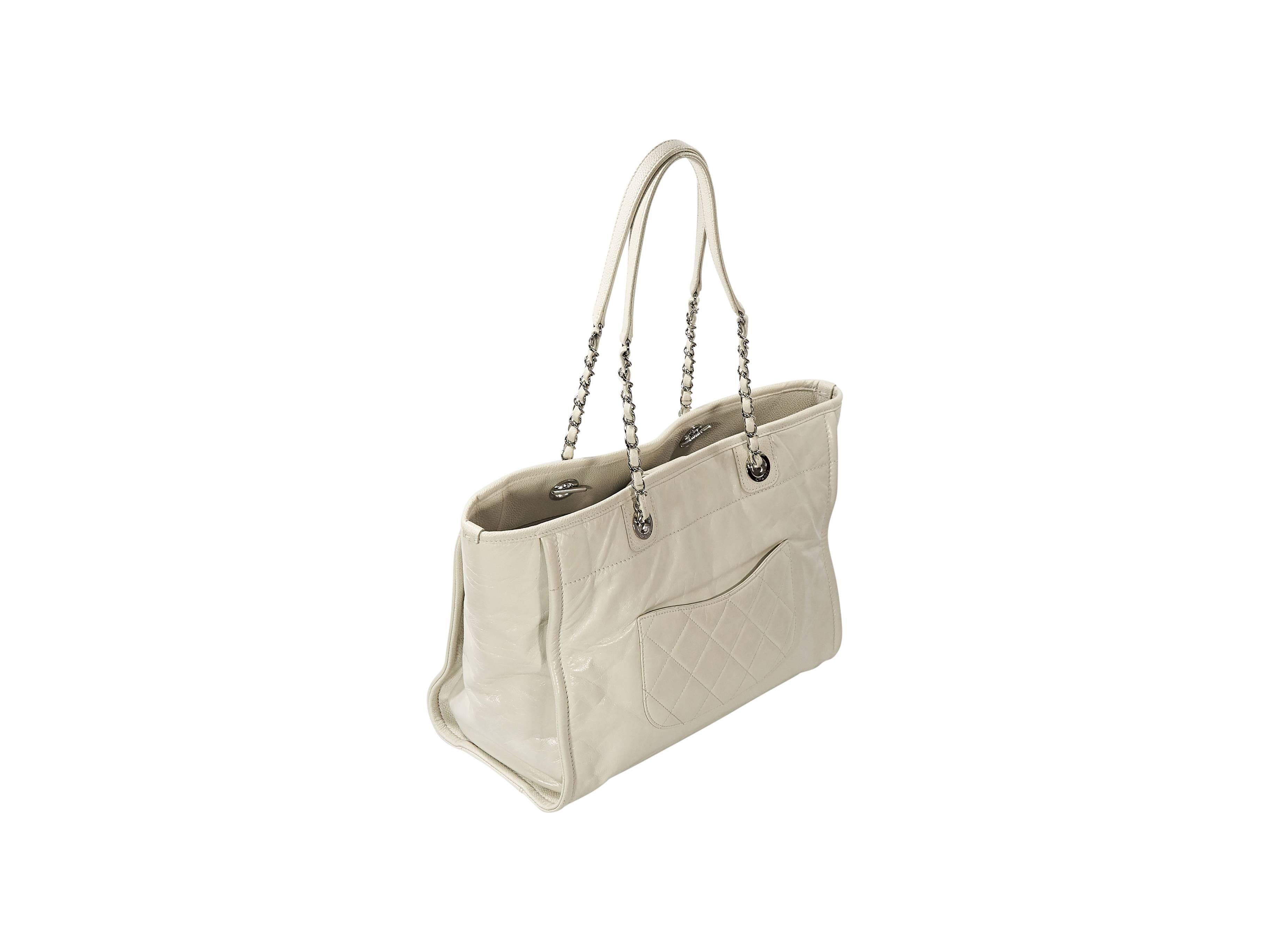 Product details: White glazed leather Deauville tote bag by Chanel. Embossed and embroidered logo front detail. Dual shoulder straps. Magnetic snap closure. Lined interior with inner zip and slide pockets plus key fob. Exterior slide half moon