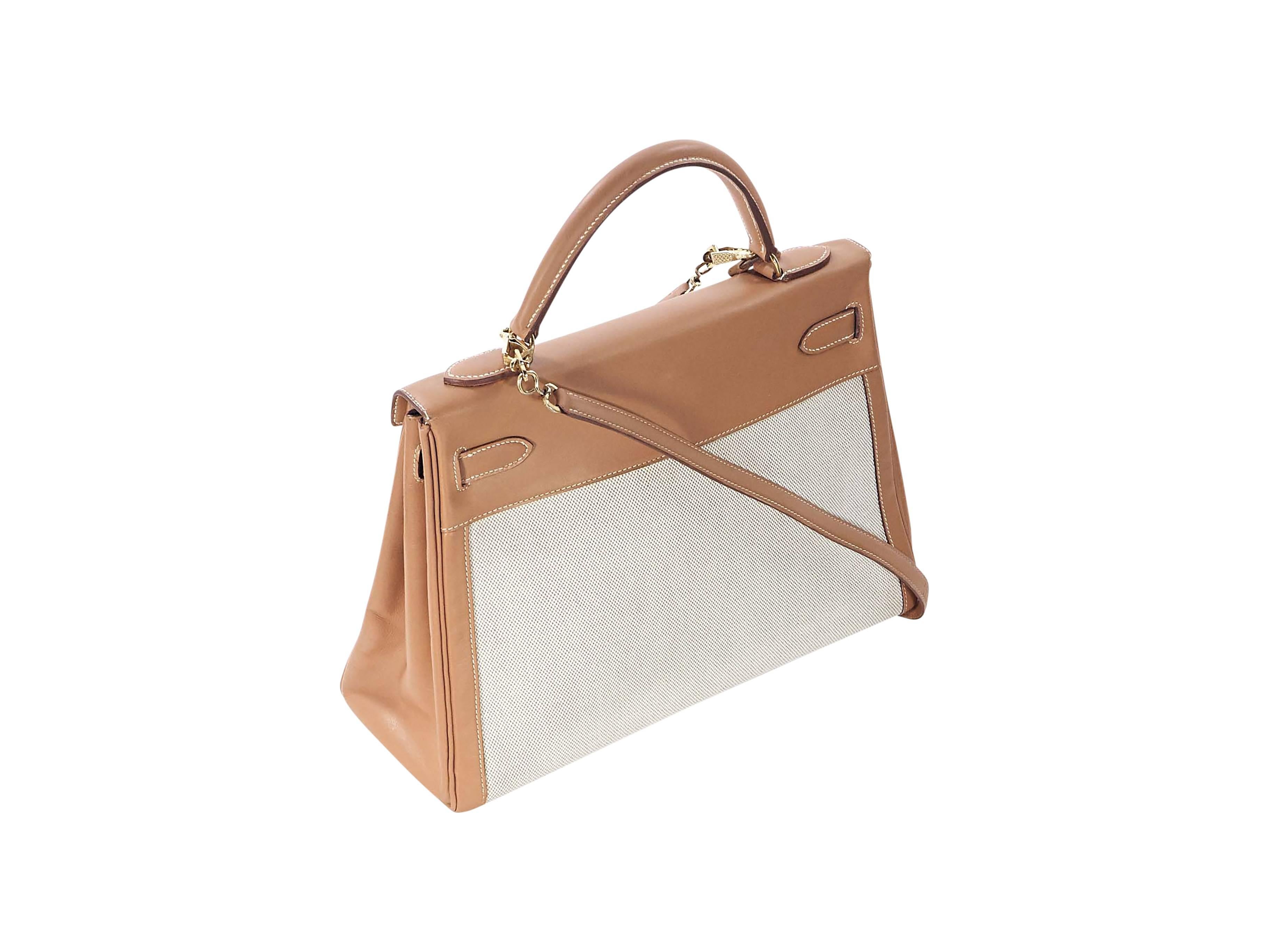 Product details: Tan leather and canvas Kelly bag by Hermès. Top carry handle. Detachable shoulder strap. Lock and key strap closure. Leather lined interior with inner zip and slide pockets. Protective metal feet. Goldtone hardware. 
Condition: Very