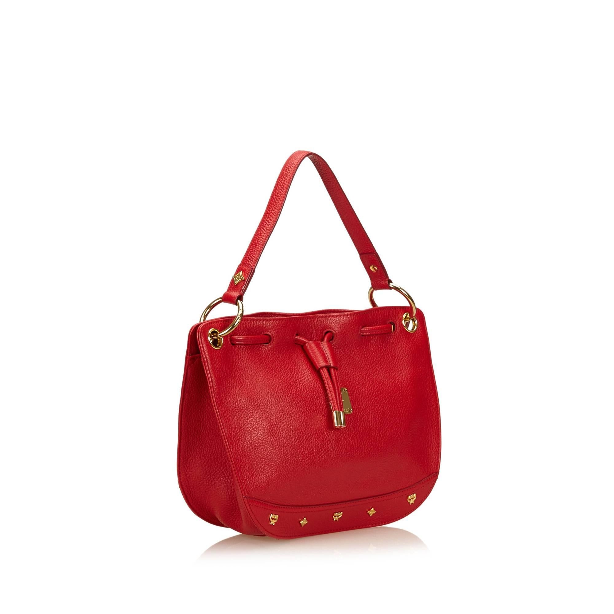 Product details:  Red pebbled leather shoulder bag by MCM.  Accented with logo plaque and studs.  Drawstring top trim.  Top carry handle.  Detachable crossbody strap.  Magnetic snap closure.  Lined interior with inner slide and zip pockets. 