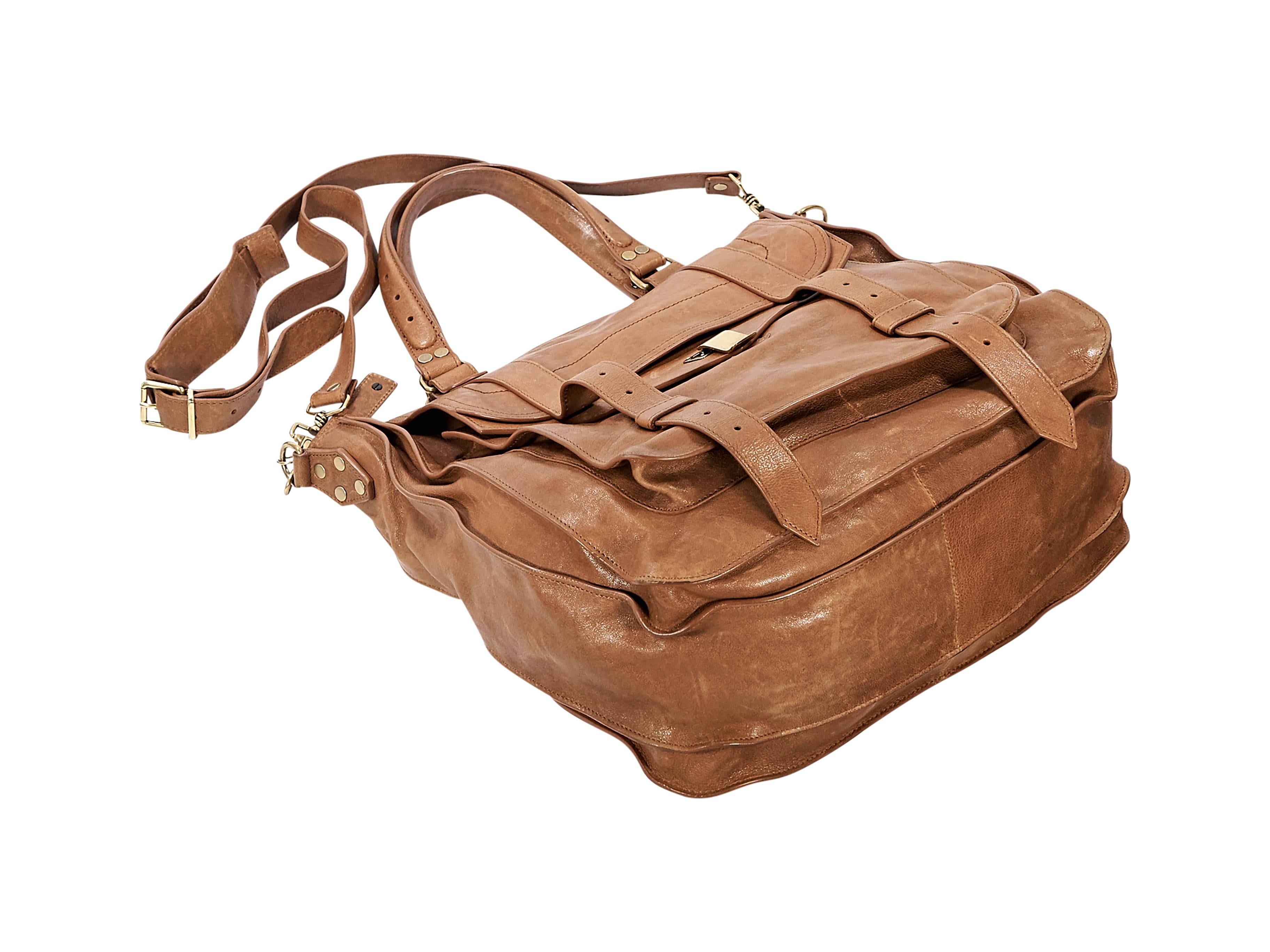 Product details: Tan leather PS1 satchel bag by Proenza Schoulder. Dual carry handles. Detachable, adjustable shoulder strap. Top zip closure. Front exterior flap pocket with flip-lock closure and buckle straps. Lined interior with inner slide and