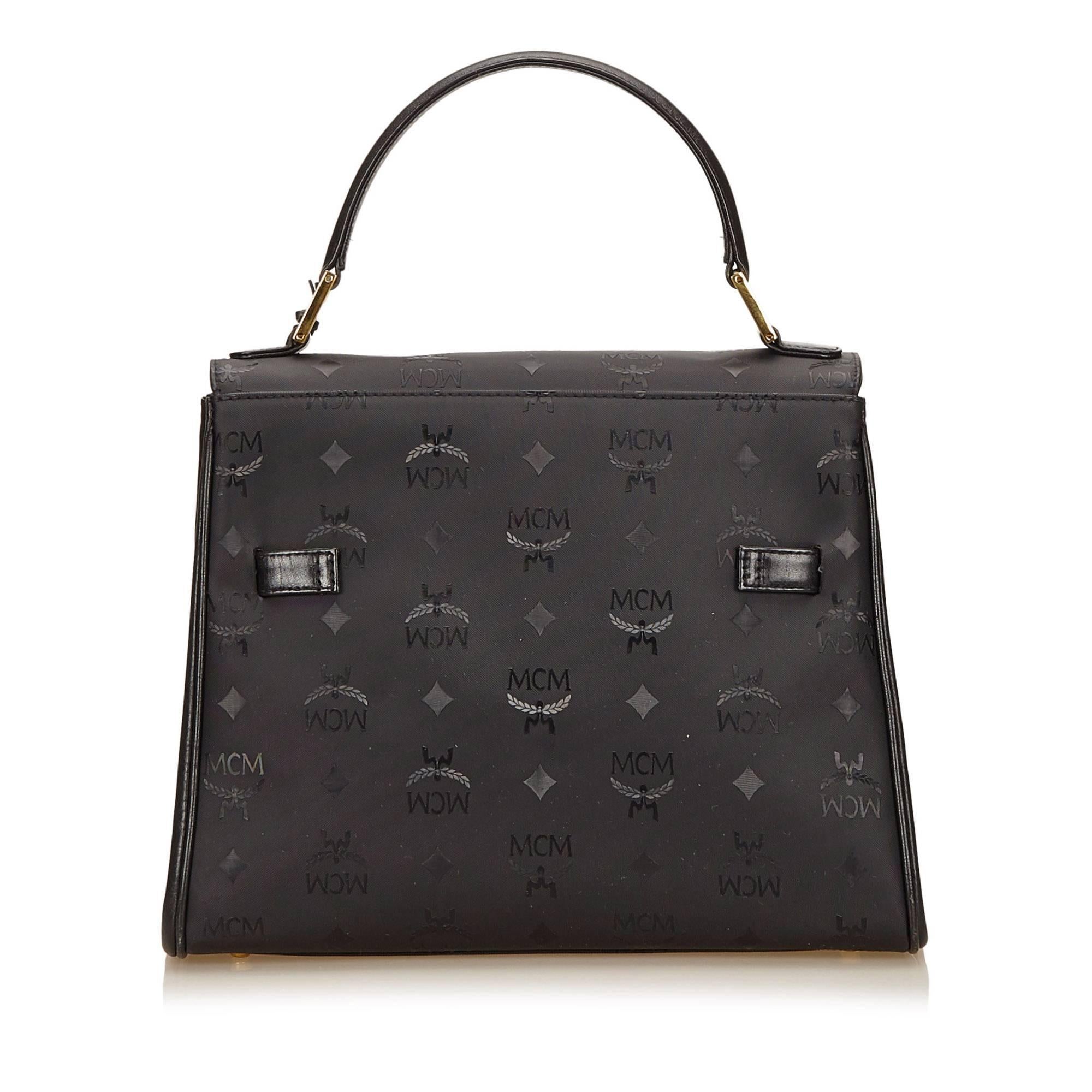 Product details: Black PVC top handle Visetos bag by MCM. Accented with tonal logo details. Top carry handle. Front flap with twist-lock closure and lock and key. Leather lined interior with inner open compartments and zip and slide pockets.
