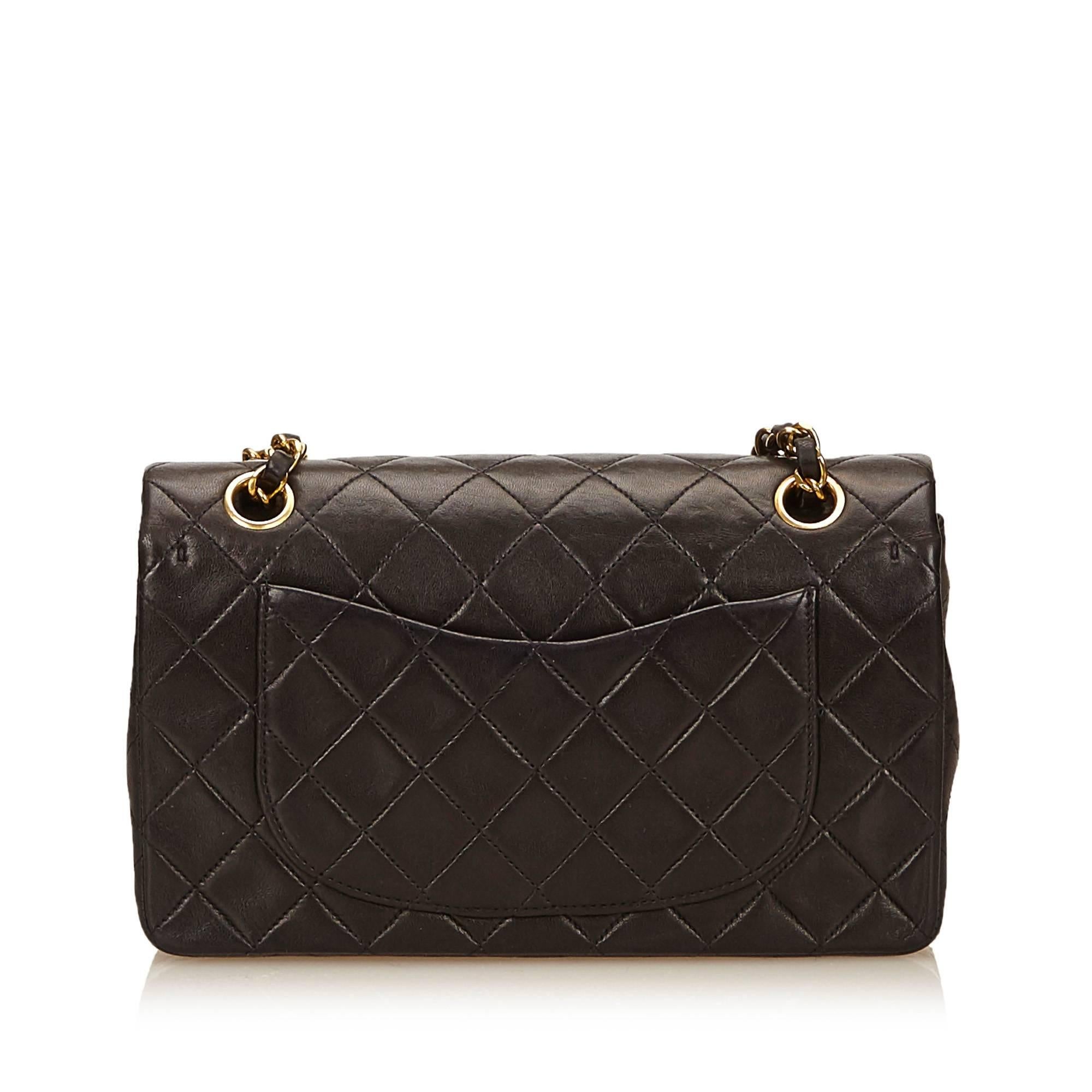 Product details: Black quilted lambskin leather double flap shoulder bag by Chanel. Front flap with twist-lock logo closure. Leather lined interior with inner slide and zip pockets. Back exterior slide pocket. Goldtone hardware. Authenticity card