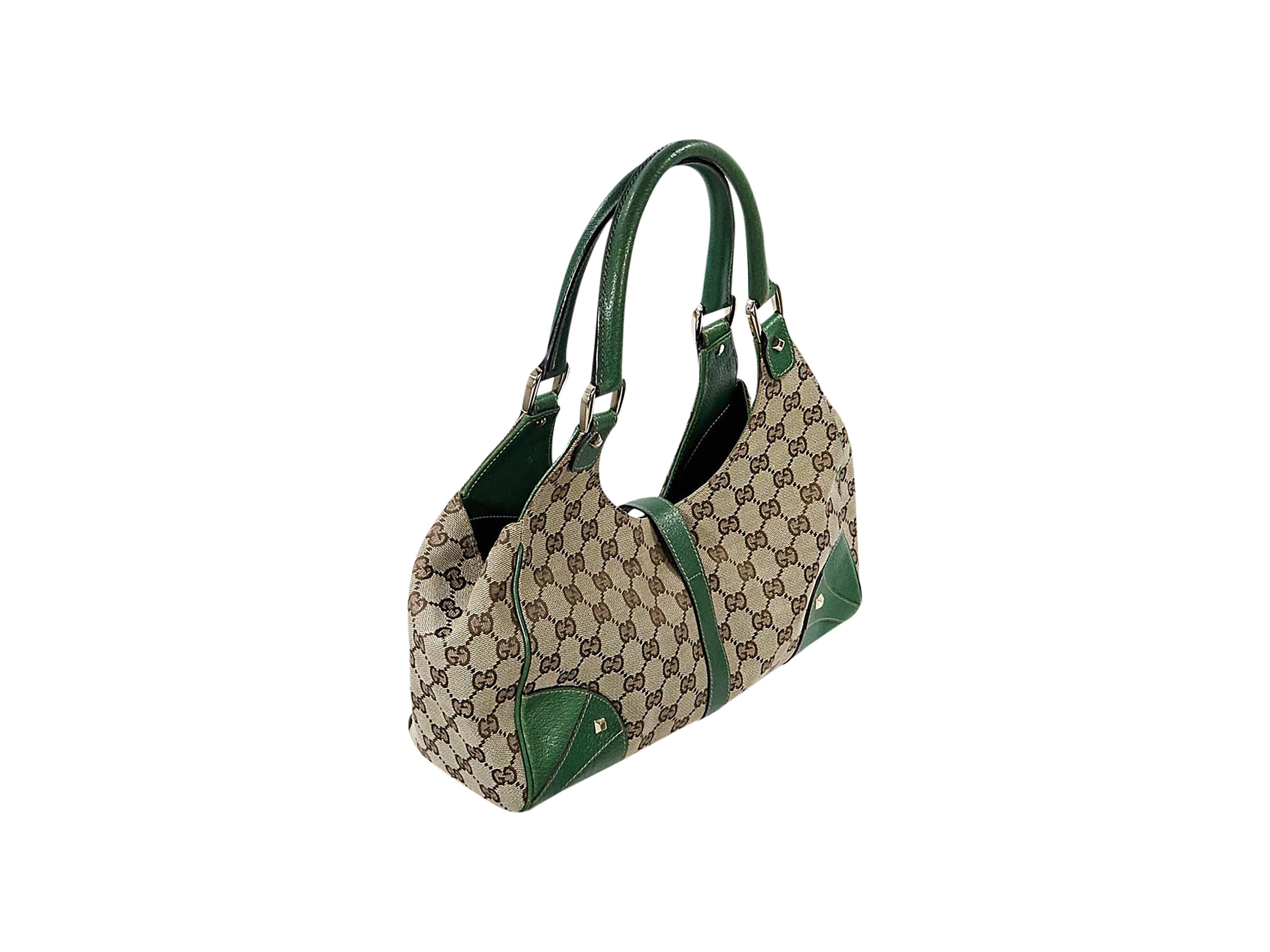 Product details: Tan GG logo Jackie shoulder bag by Gucci. Accented with green leather. Dual shoulder straps. Push-lock clasp closure. Lined interior with inner zip pocket. Protective metal feet. Goldtone hardware. 14