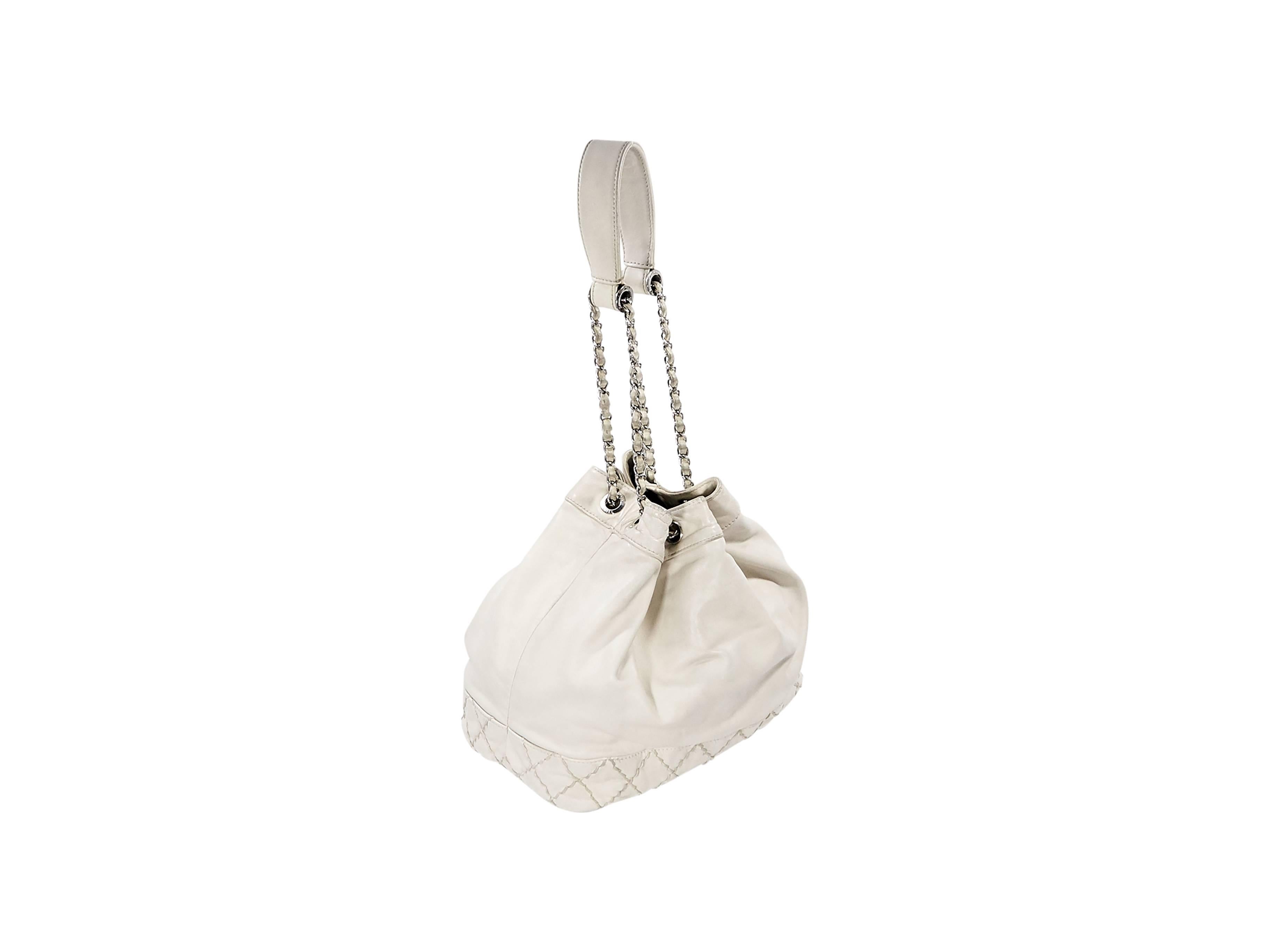Product details:  Ivory leather quilted Surpique bucket bag by Chanel.  Front topstitched CC logo.  Single shoulder strap.  Drawstring top closure.  Lined interior with inner zip and slide pockets and a key fob.  Protective metal feet.  Silvertone